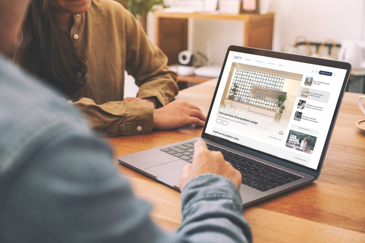 Duas pessoas olhando a página inicial do Archtrends na tela de um laptop. Seus rostos não aparecem na imagem