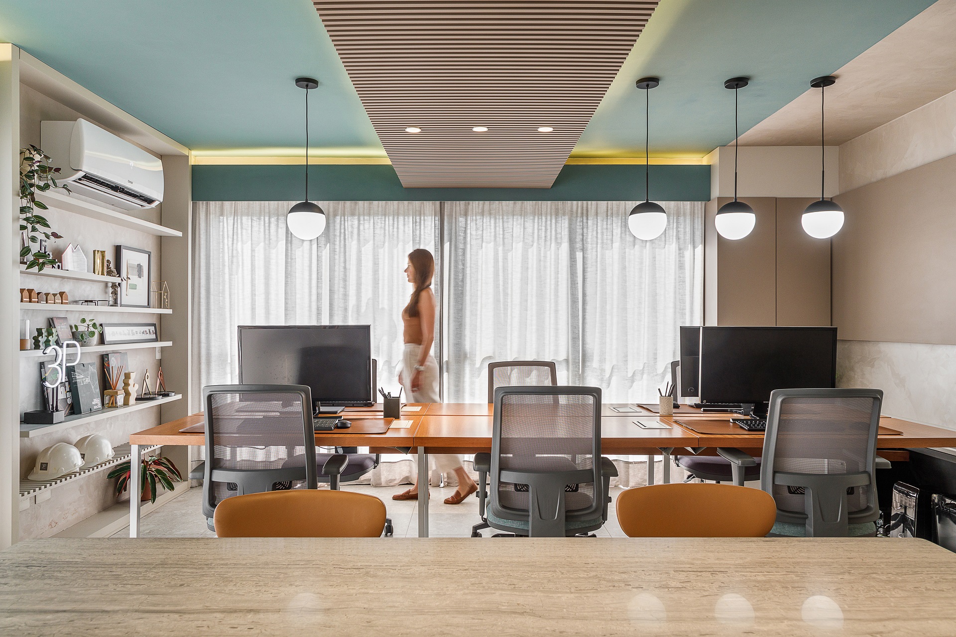 Mulher atravessando um escritório de arquitetura com mesas, cadeiras e prateleiras