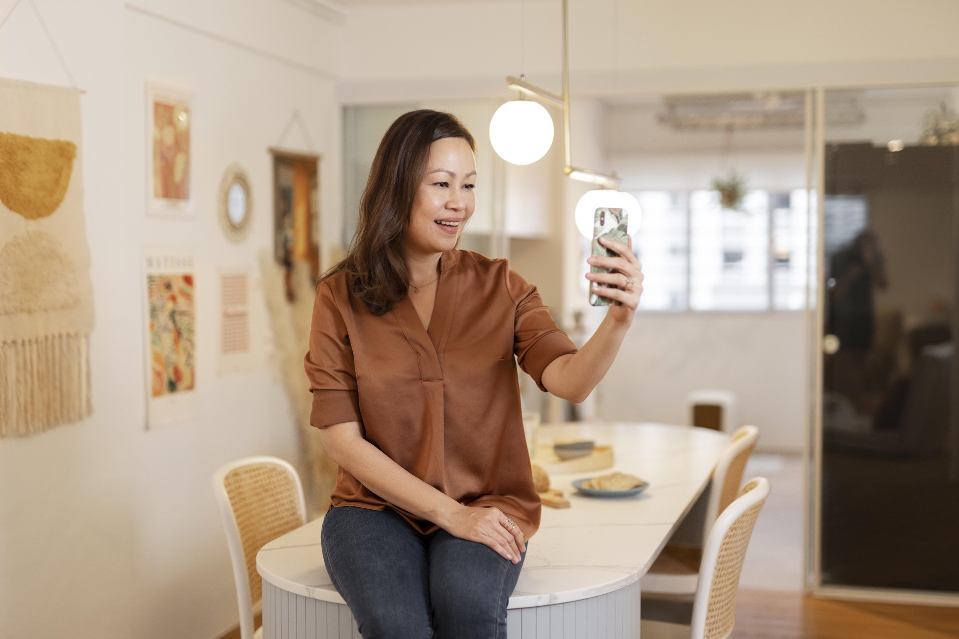 Mulher sentada em uma mesa. Ela parece estar criando um conteúdo no seu celular