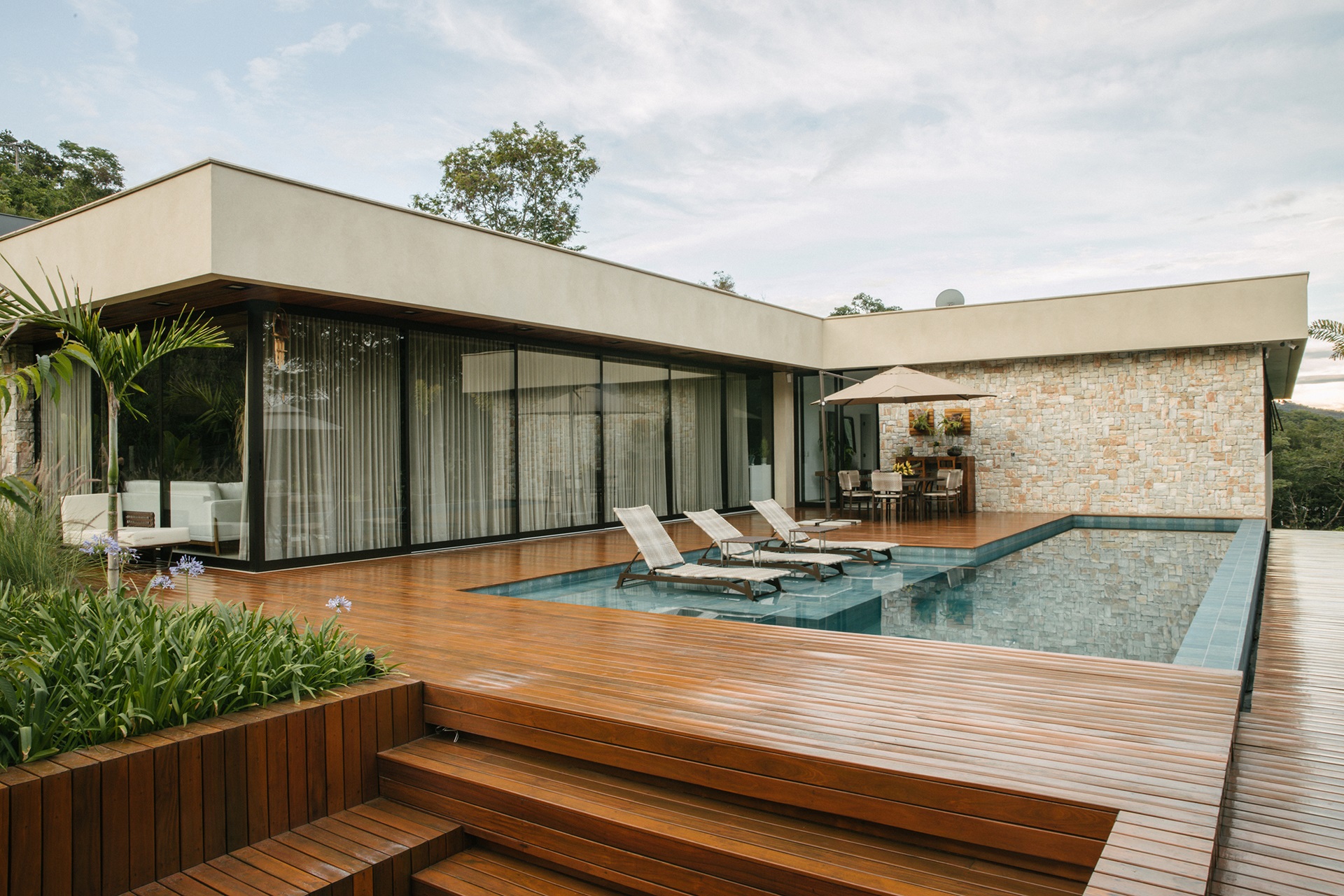 Piscina com deck molhado em tom esverdeado e piso de madeira no entorno
