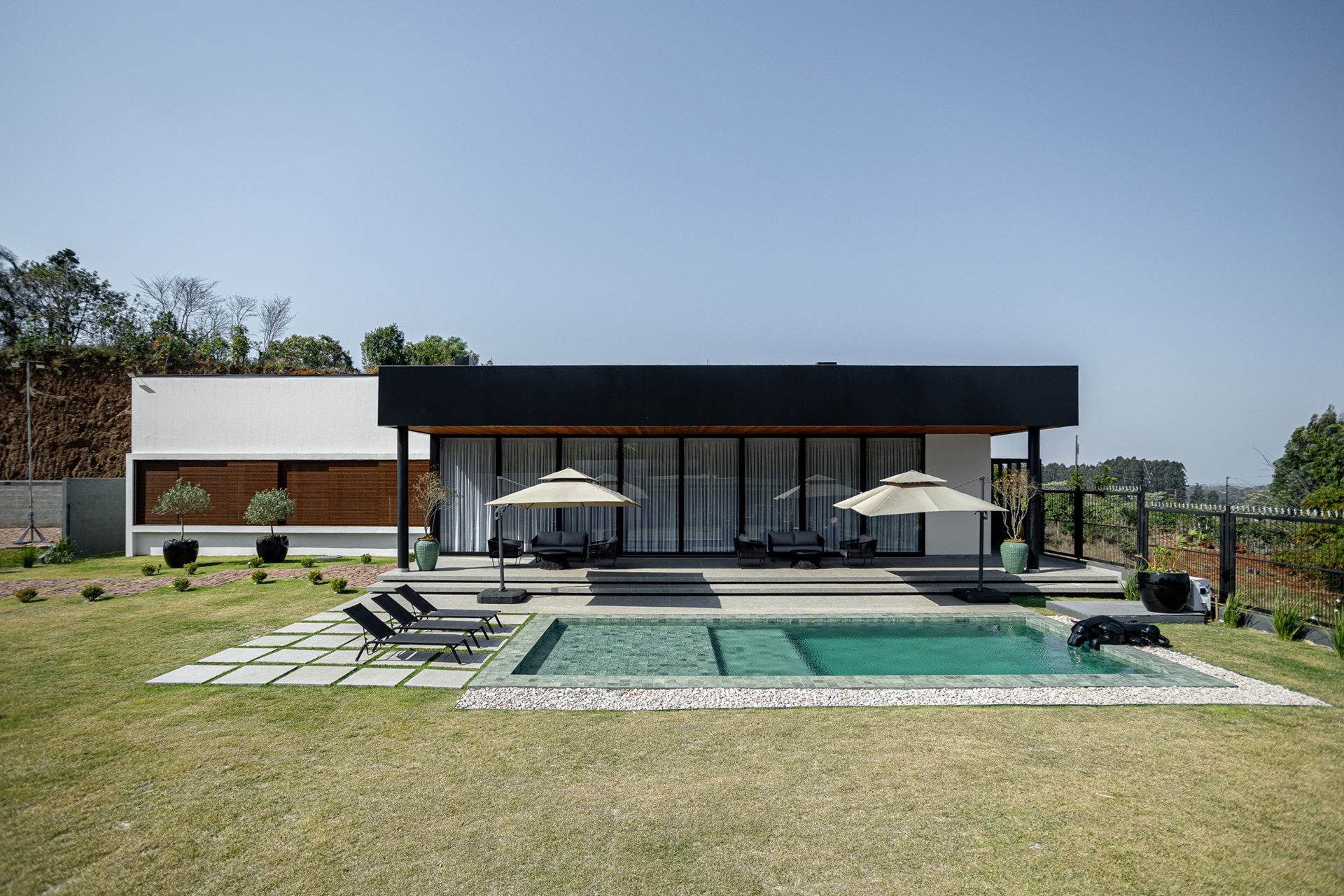 Vista de longe de piscina em alvenaria com deck molhado e casa contemporânea linear ao fundo