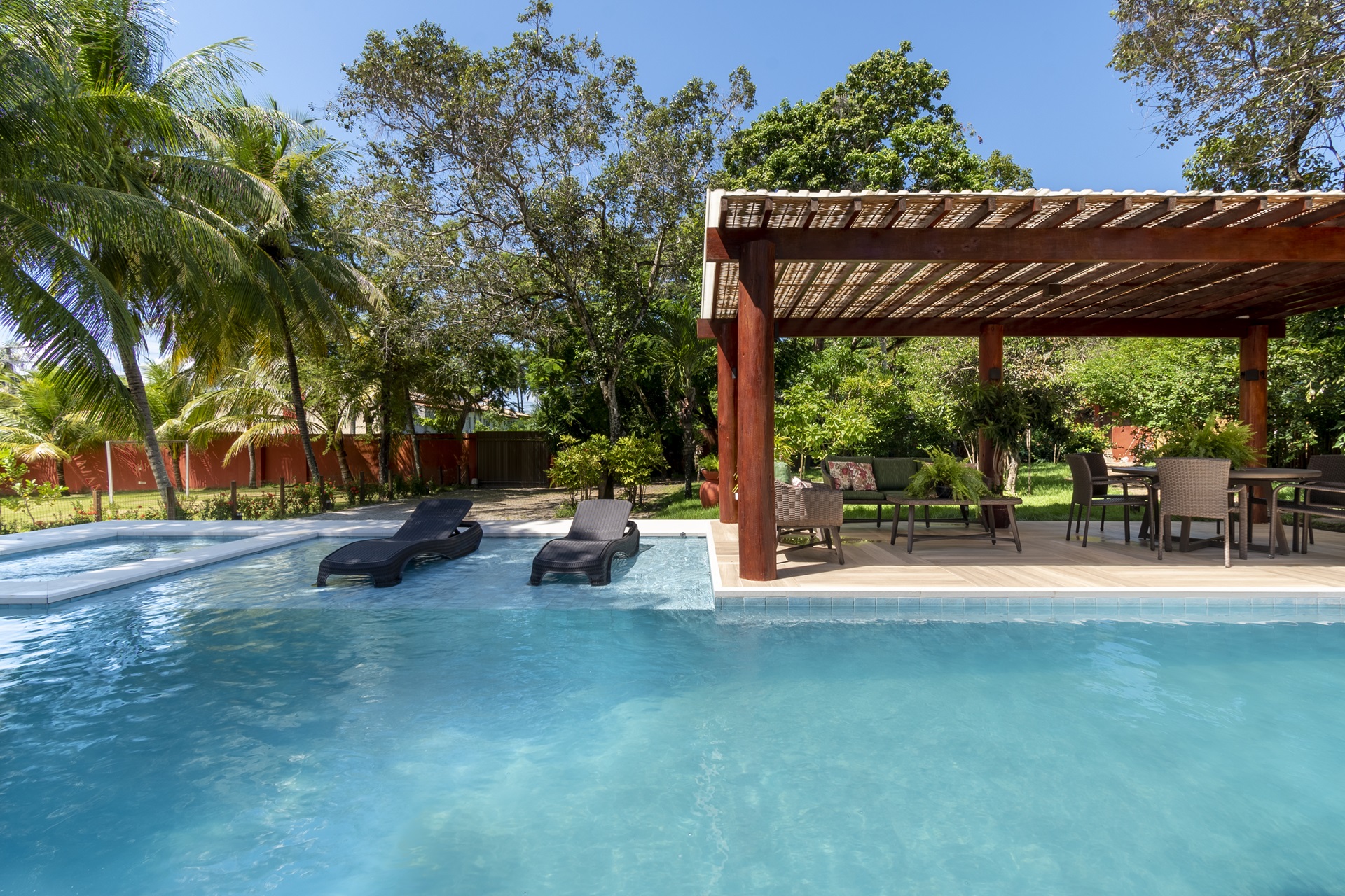 Piscina com revestimento azul e deck molhado com duas espreguiçadeiras ao lado de área coberta com poltronas
