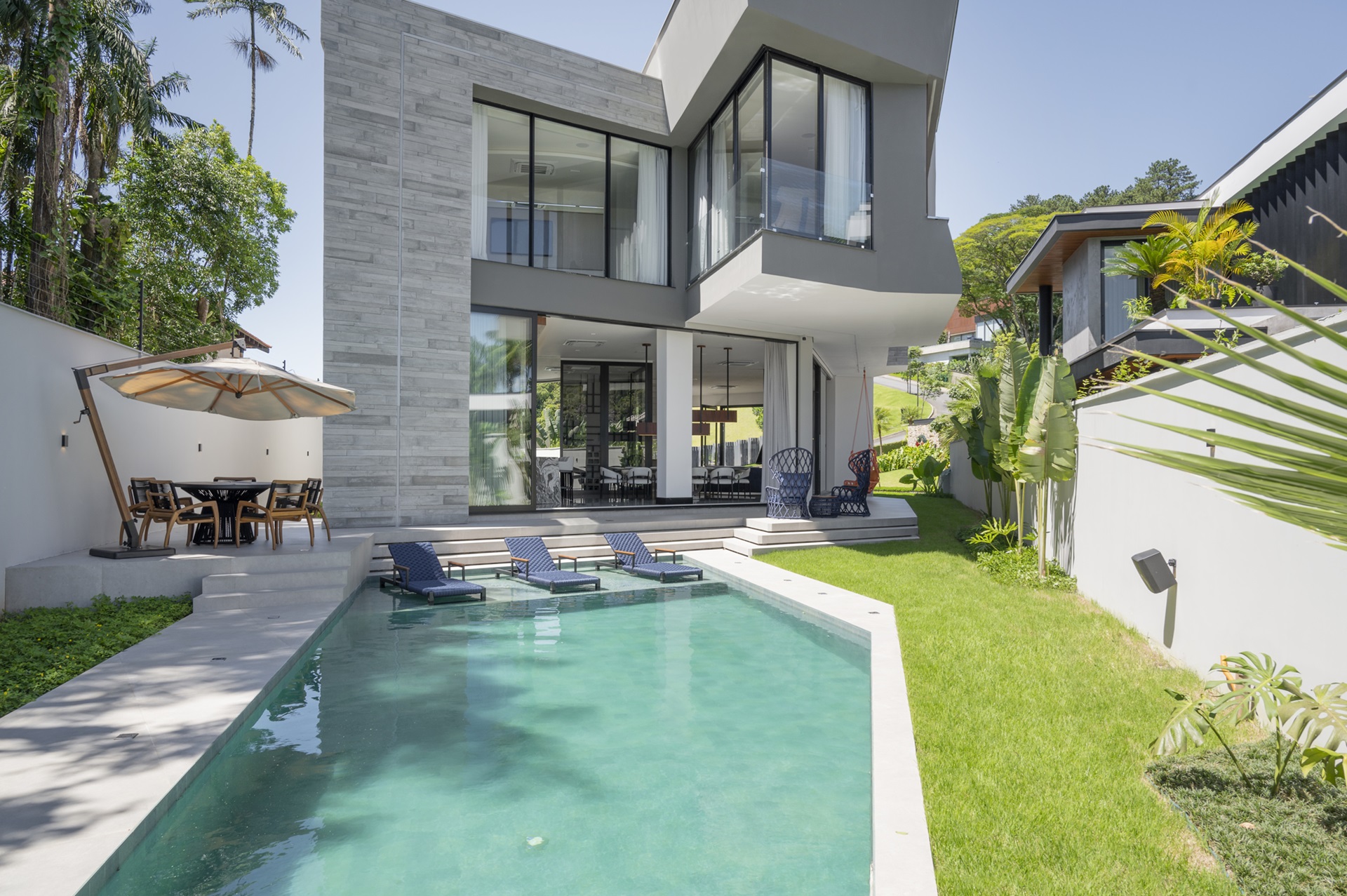 Piscina com revestimento verde com casa contemporânea de dois andares ao fundo