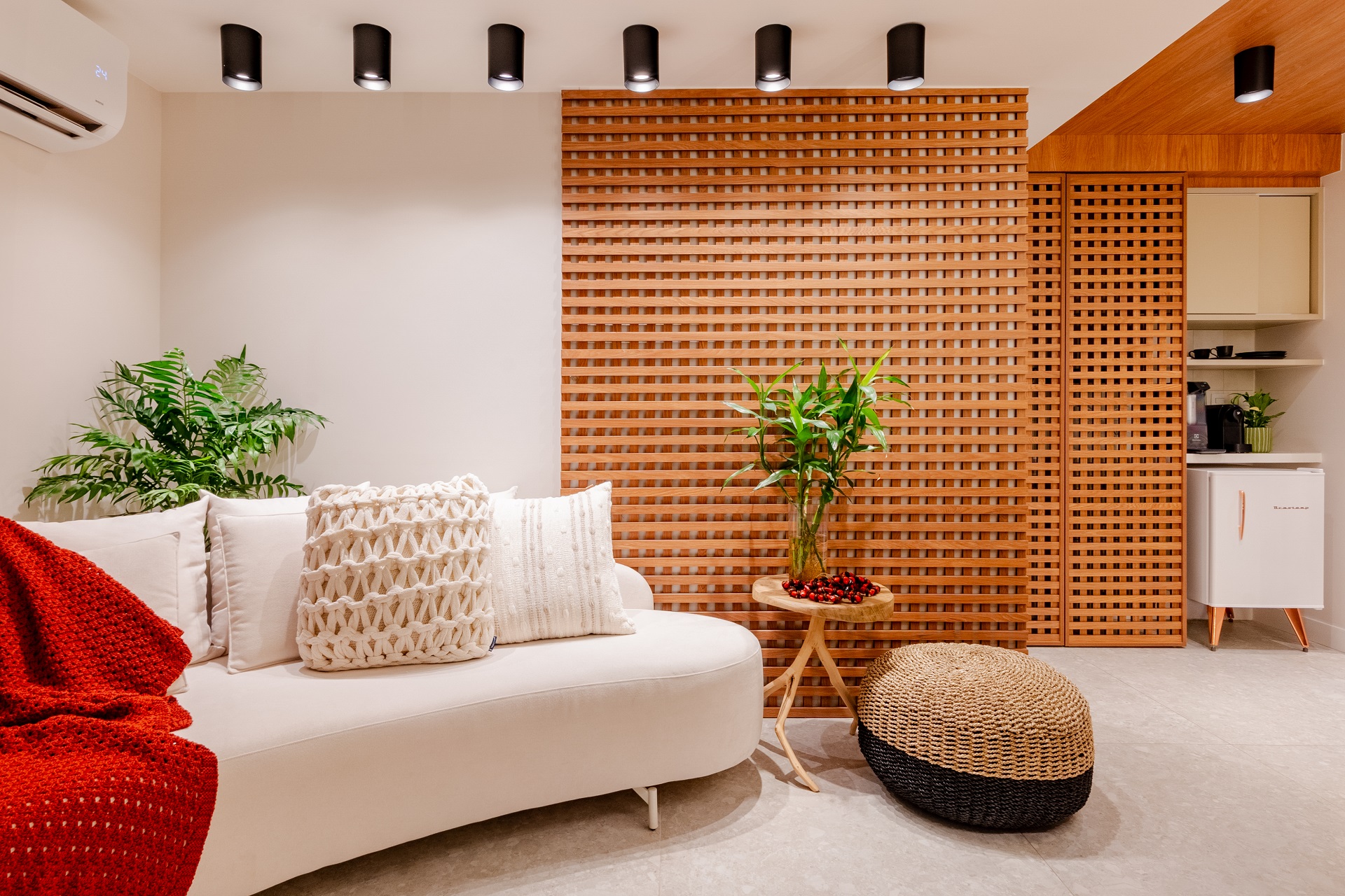 Detalhe de ambiente com sofá em forma orgânica e mesinha. Predominam os tons terrosos, as matérias-primas naturais e as plantas