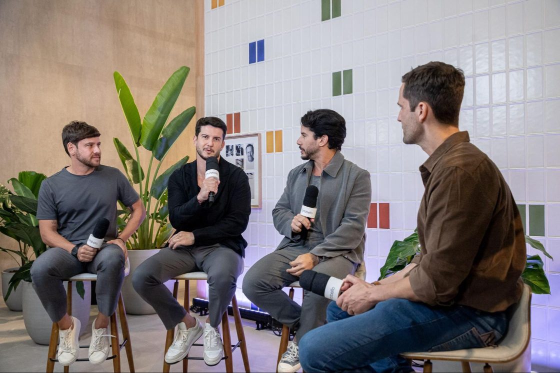 Fotografia de quatro homens conversando sentados à frente de um painel de azulejos e vasos de plantas