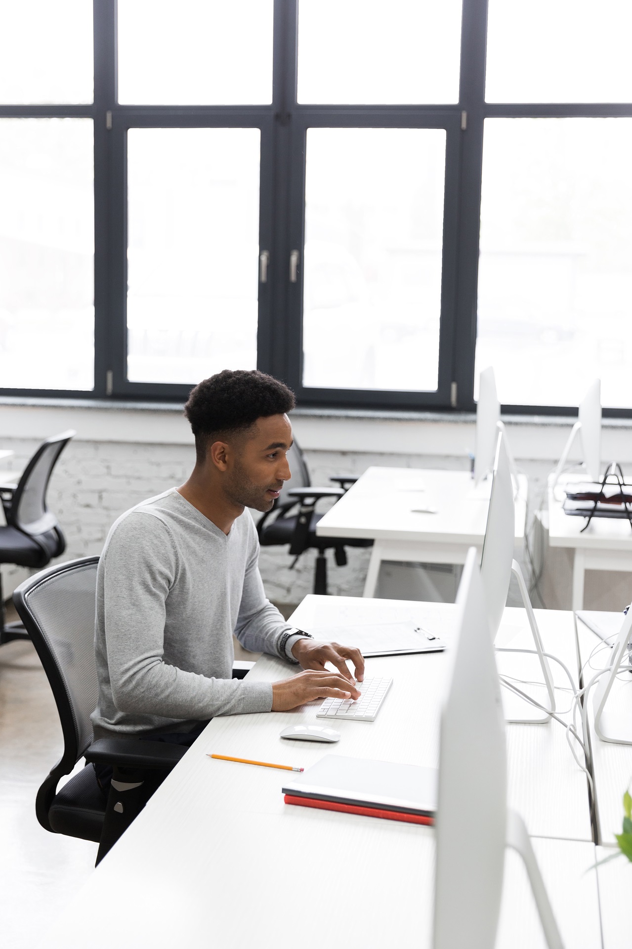 Homem trabalhando em um computador de mesa (desktop). Ele está em um ambiente em estilo industrial
