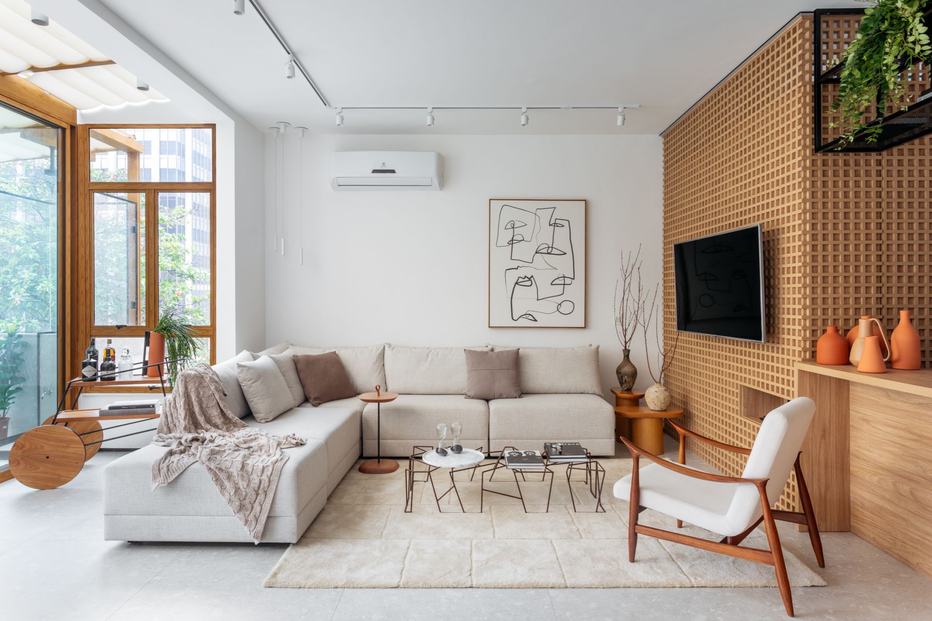 Sala de estar em tons neutros, com sofá, mesinhas, cadeira, TV e quadro