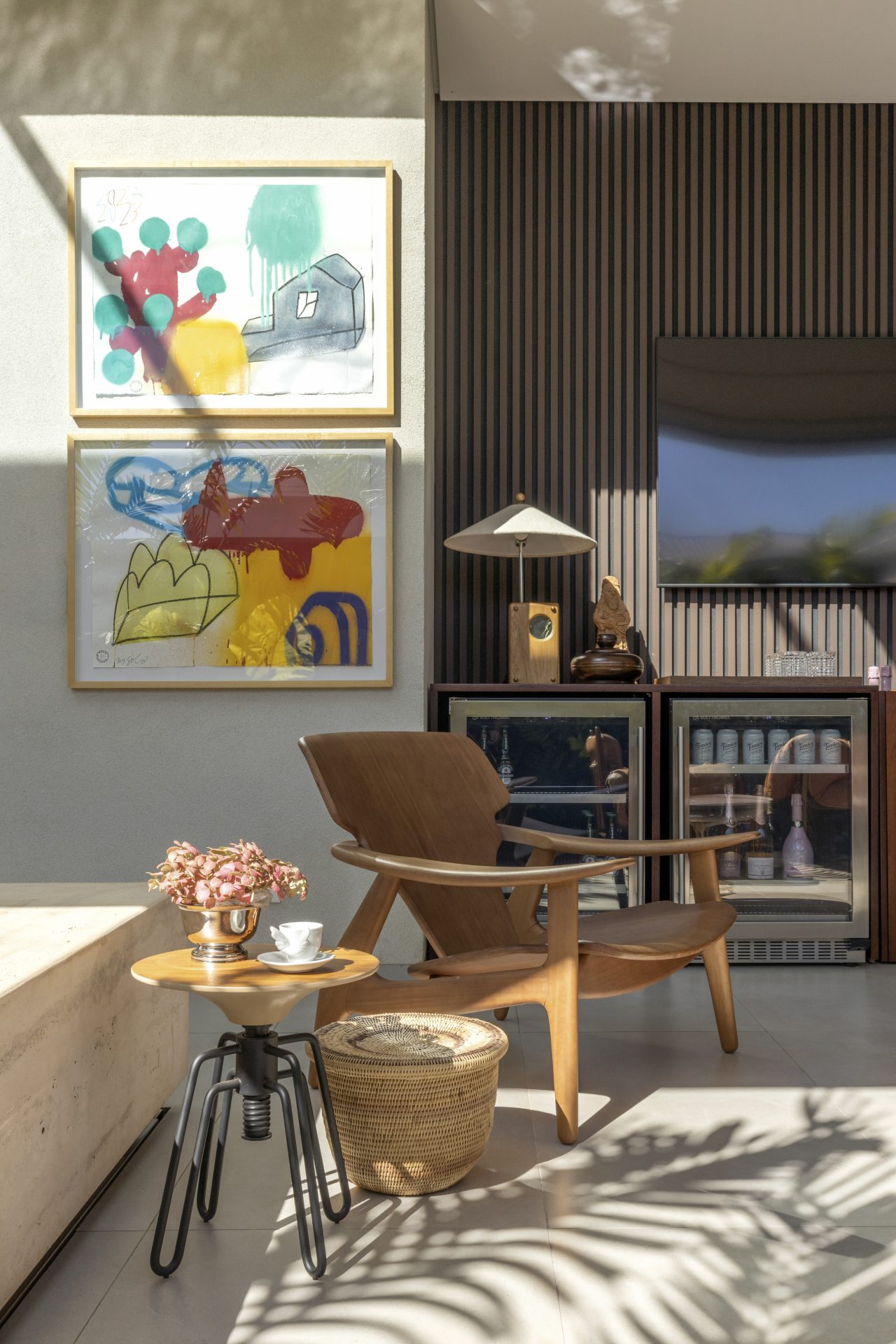 Detalhe de ambiente com cadeira, mesa, painel de TV, adega e quadros