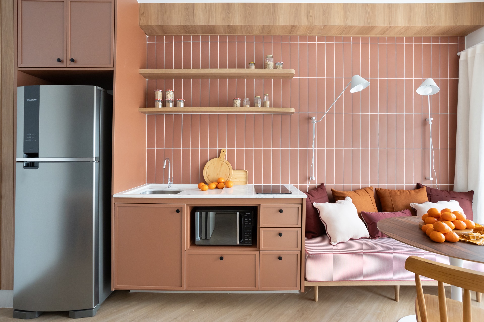 Cozinha compacta com móveis e parede terracota e sofá com mesa de jantar em frente