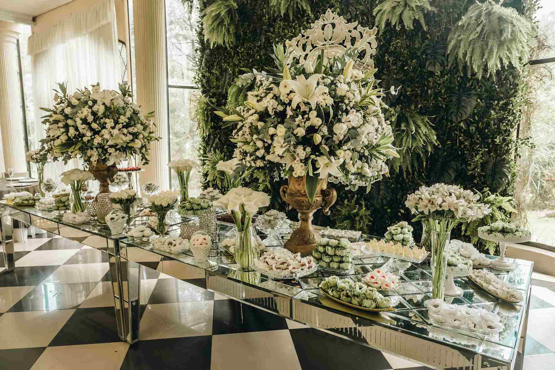 Mesa de doces em casamento, com folhagens e flores brancas