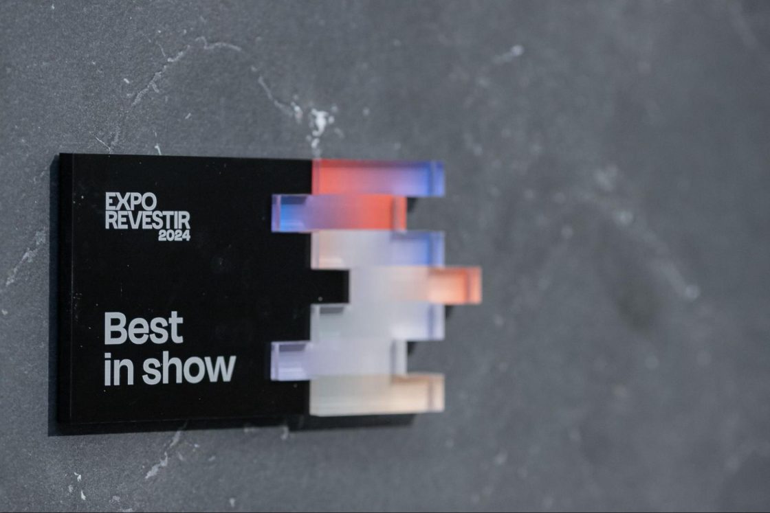 Placa preta em parede cinza com inscrição do prêmio Best in Show, na Expo Revestir 2024