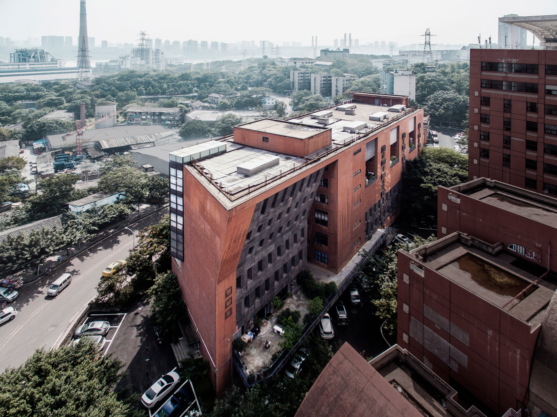 Vista aérea do Departamento de Escultura do Instituto de Belas Artes de Sichuan, um edifício moderno com um design arquitetônico distinto. A estrutura combina concreto cinza e um tom avermelhado, com uma fachada inclinada e janelas dispostas de forma irregular