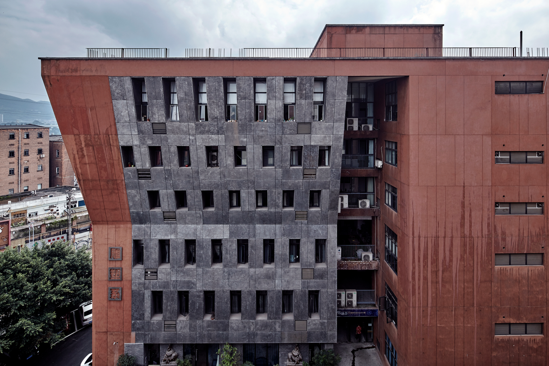 Departamento de Escultura do Instituto de Belas Artes de Sichuan, um edifício com uma arquitetura assimétrica. A fachada é composta por uma combinação de concreto cinza e uma estrutura avermelhada, com um design inclinado e janelas