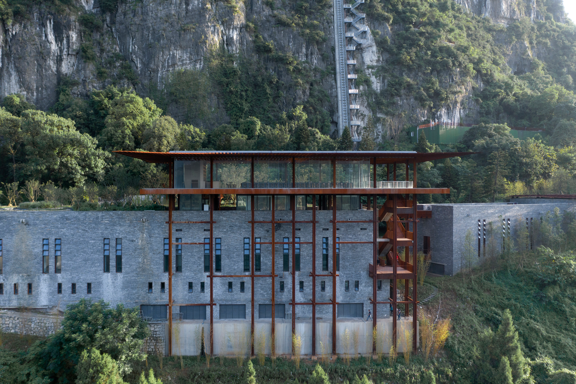 Tianbao Cave, estrutura arquitetônica integrada ao ambiente natural de um penhasco. O edifício combina materiais modernos, como aço e vidro, com pedras