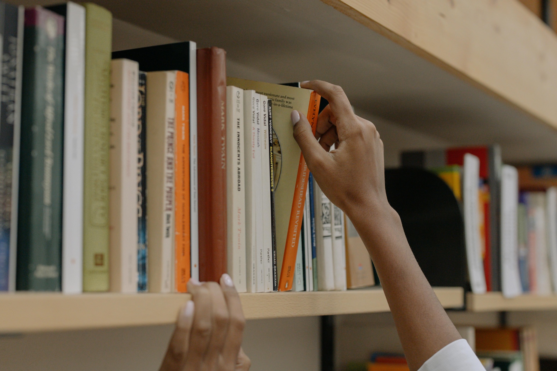 Pessoa pegando livro em prateleira. O rosto dela não aparece