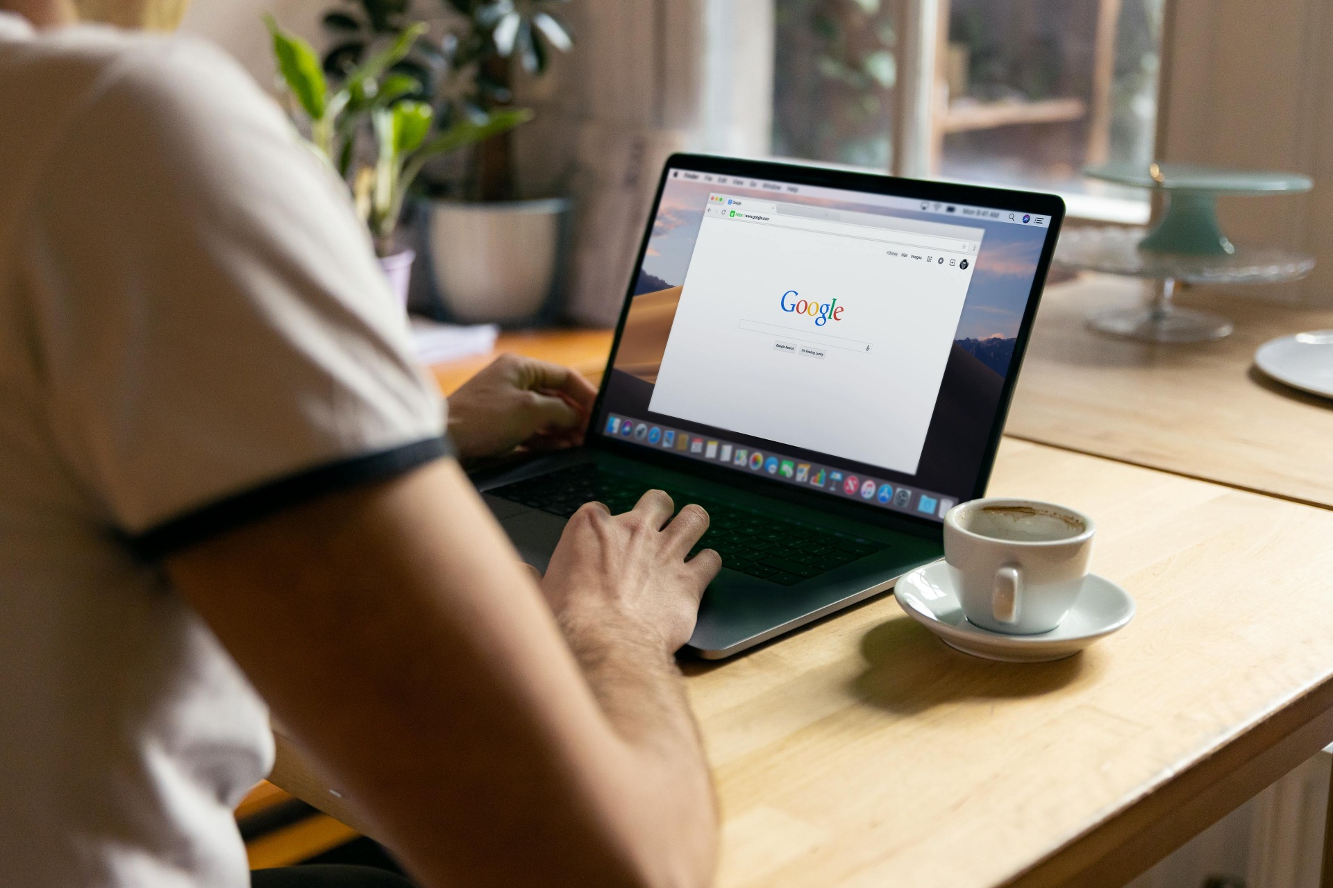 Pessoa acessando o Google pelo laptop. Seu rosto não aparece. Ao lado do aparelho há uma xícara