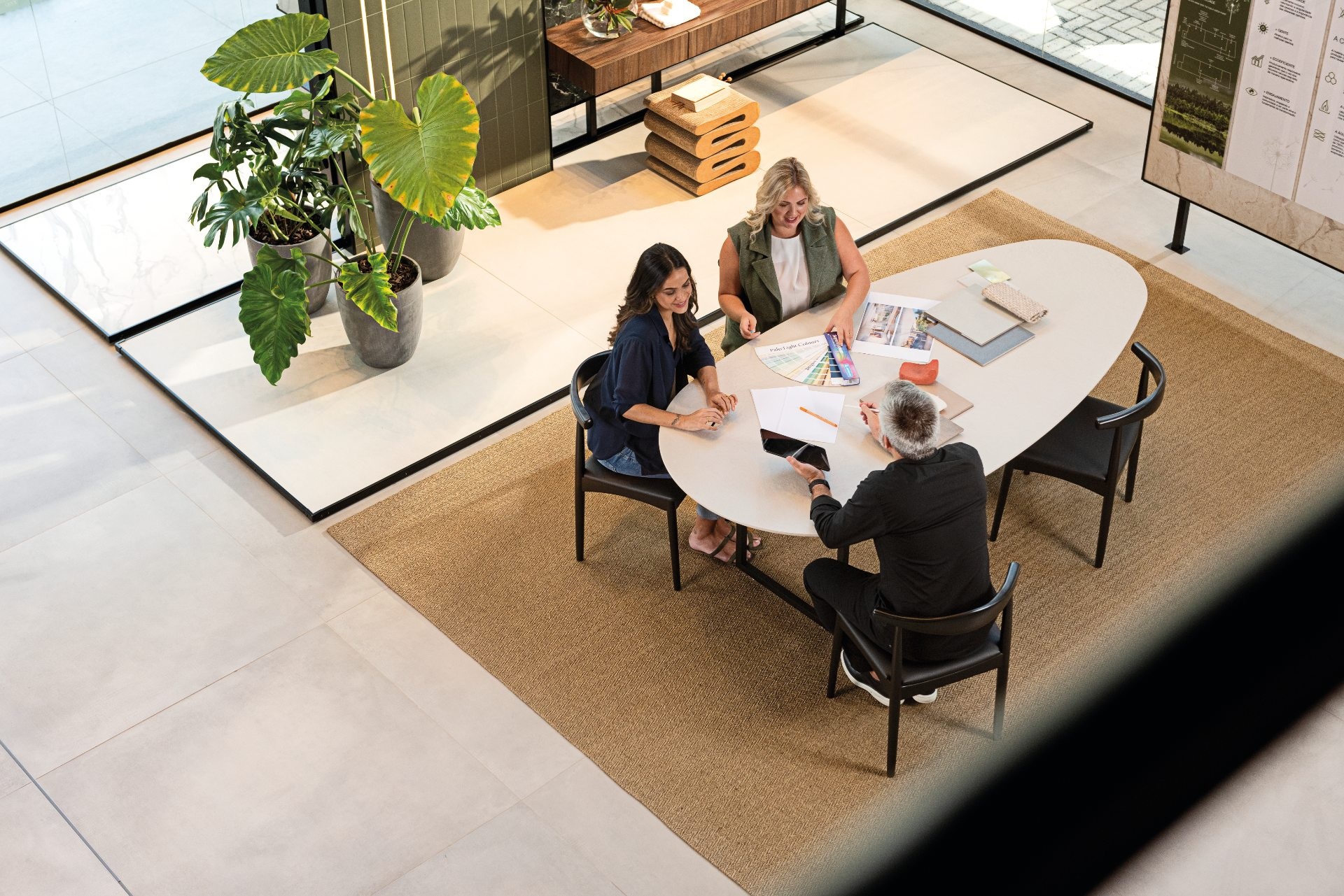 Duas mulheres e um homem sentados ao redor de uma mesa em forma orgânica. Eles parecem estar conversando sobre um projeto de arquitetura