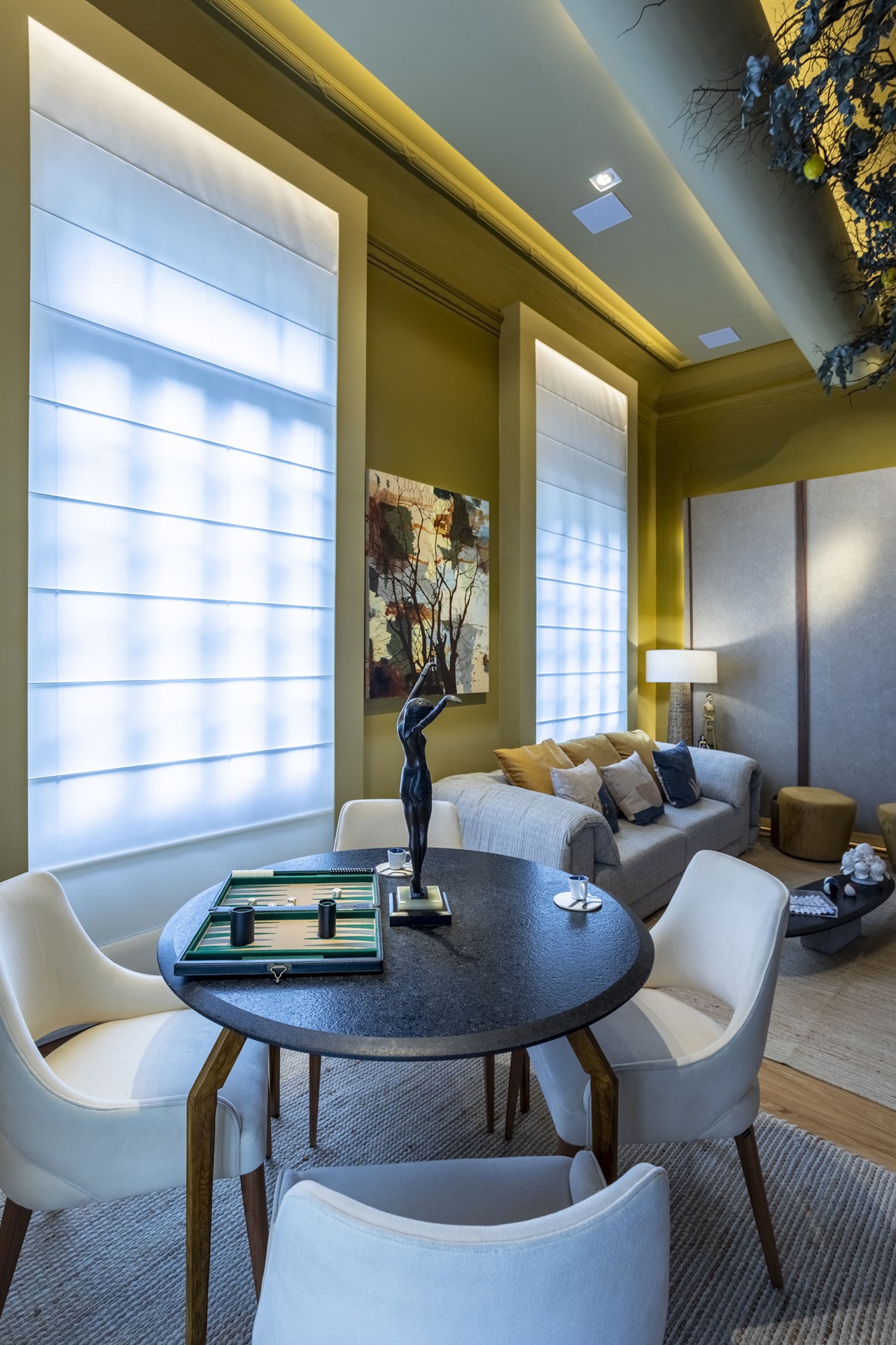 Living com decoração que faz contraste entre tons claros, preto e amarelo, com mesa redonda com jogo de tabuleiro em evidência