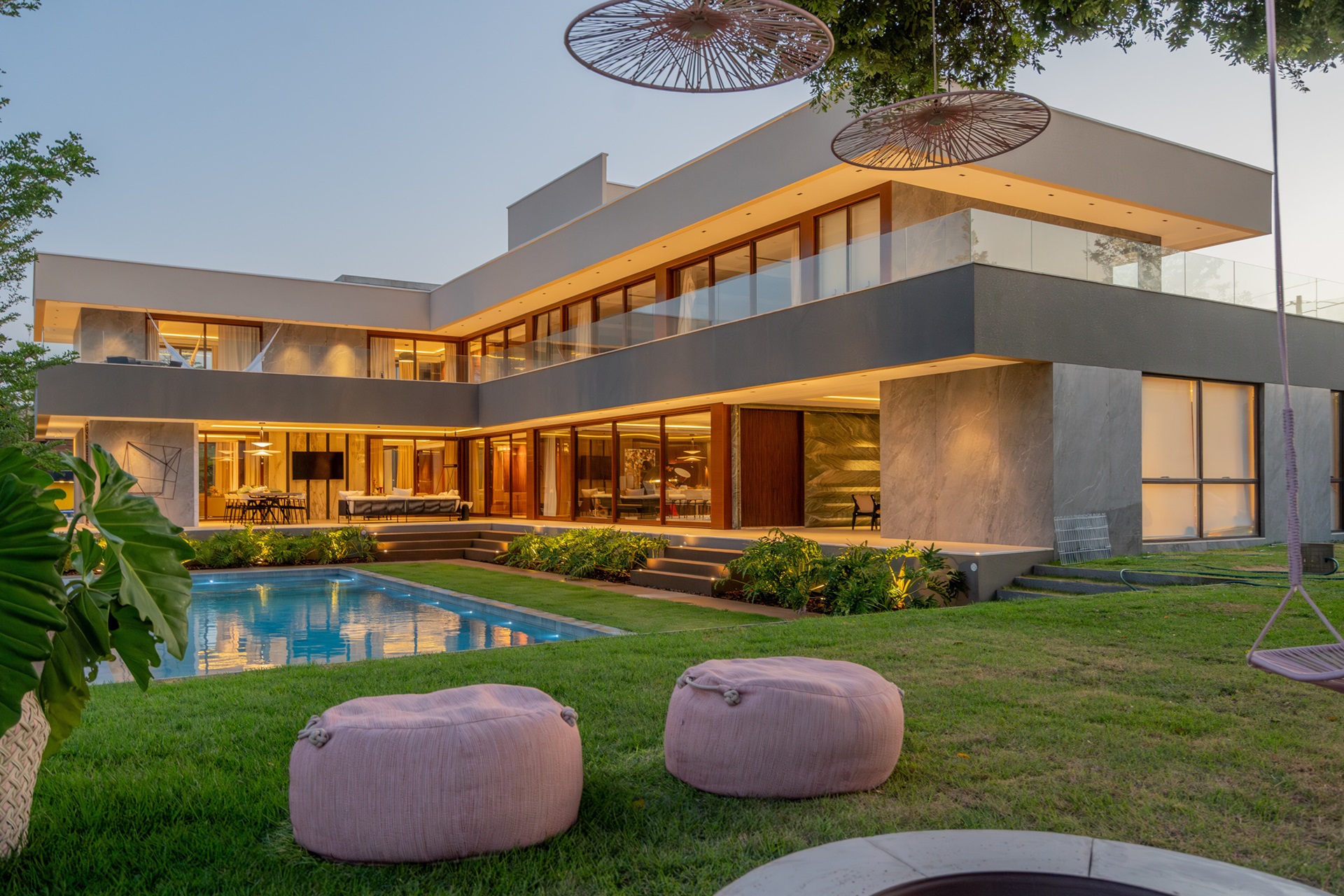 Imagem da área externa da casa, com gramado e piscina e casa em L ao fundo e do lado esquerdo