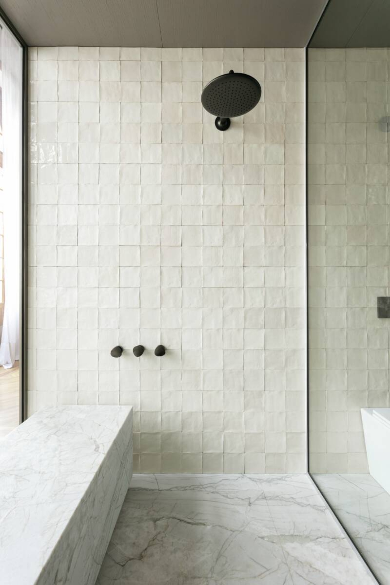 Um chuveiro preto em uma parede de azulejos brancos. Neste box, há uma bancada e de mármore