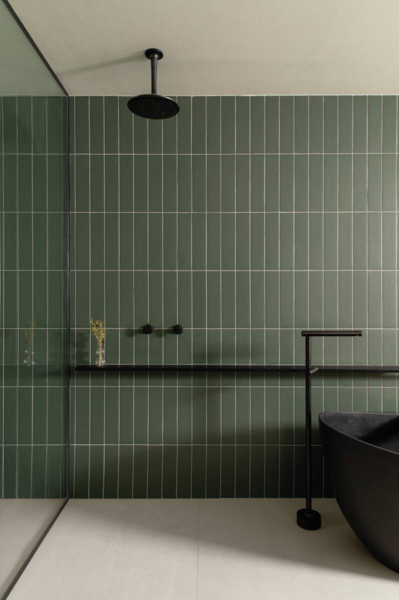 Um banheiro com uma banheira preta e um chuveiro preto acoplado em uma parede de azulejos verdes e rejunte branco