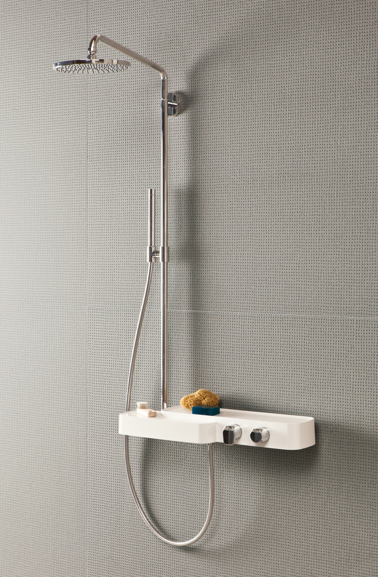 Chuveiro moderno instalado em uma parede revestida com pequenos azulejos em tom neutro. O chuveiro tem um design sofisticado, com um cabeçote redondo e amplo, além de um chuveirinho de mão acoplado a uma estrutura metálica.