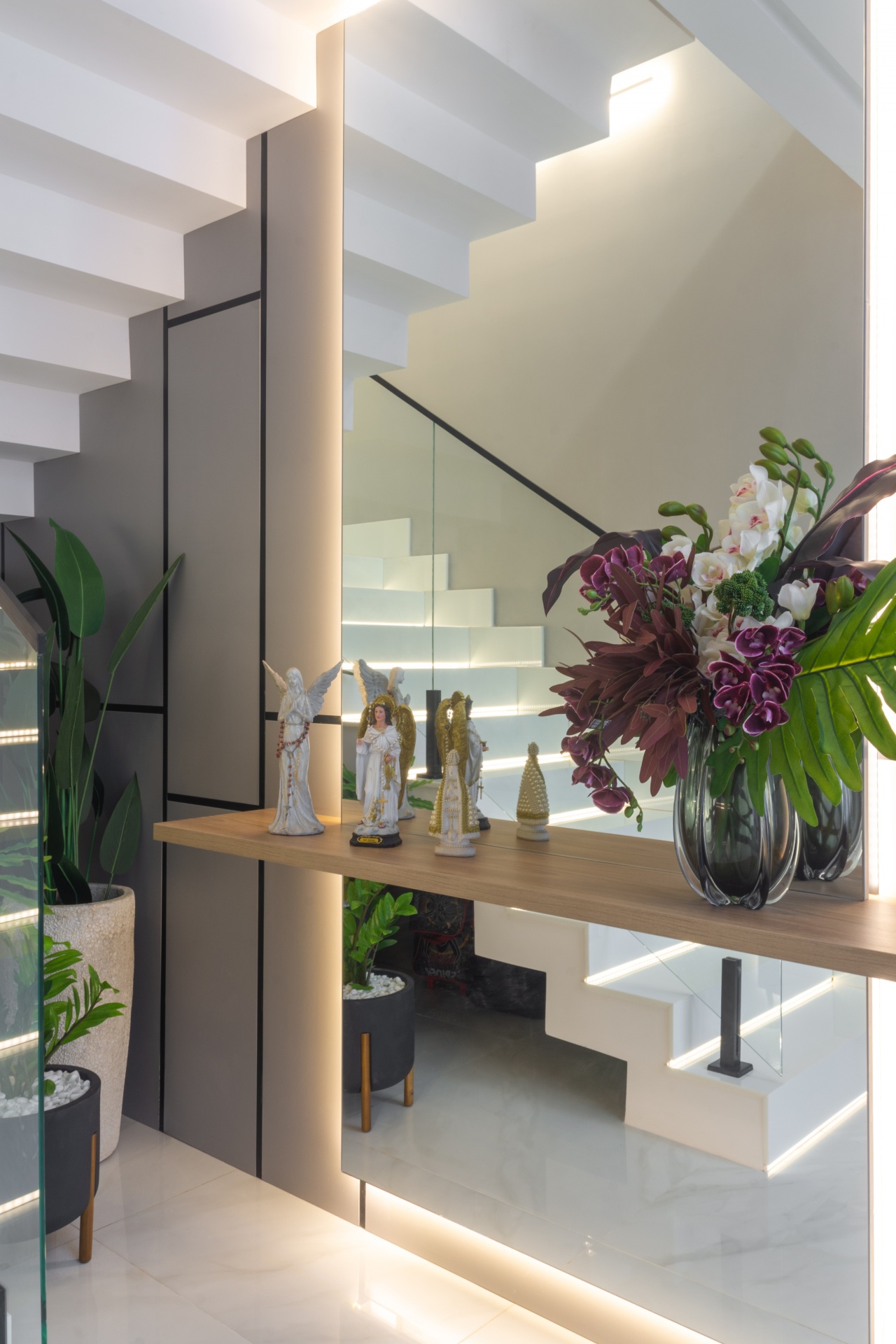 Altar sob escada, com imagens de santos, anjos e um vaso de flores