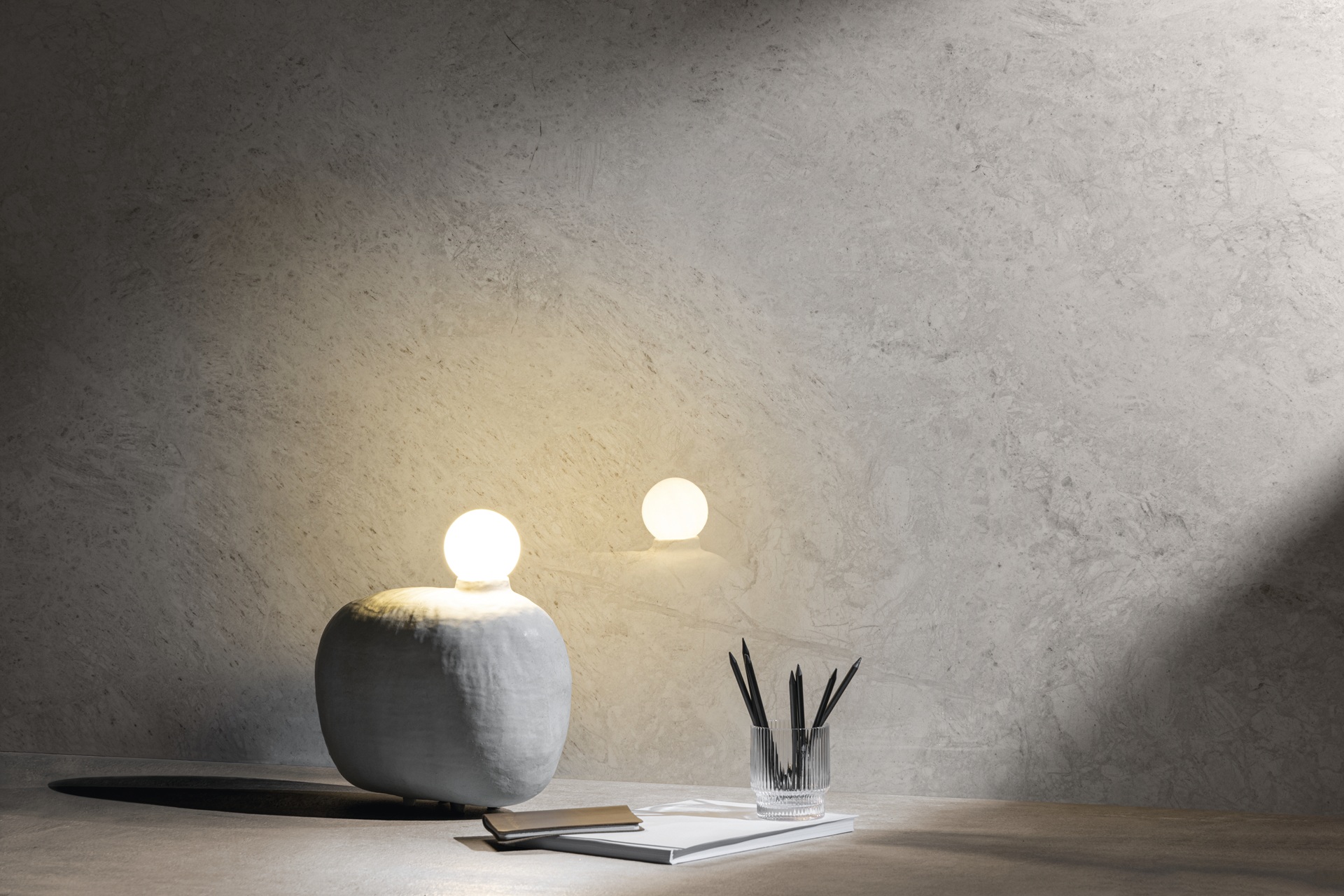 Parede em destaque com mesa em frente com luminária, porta-lápis e livro