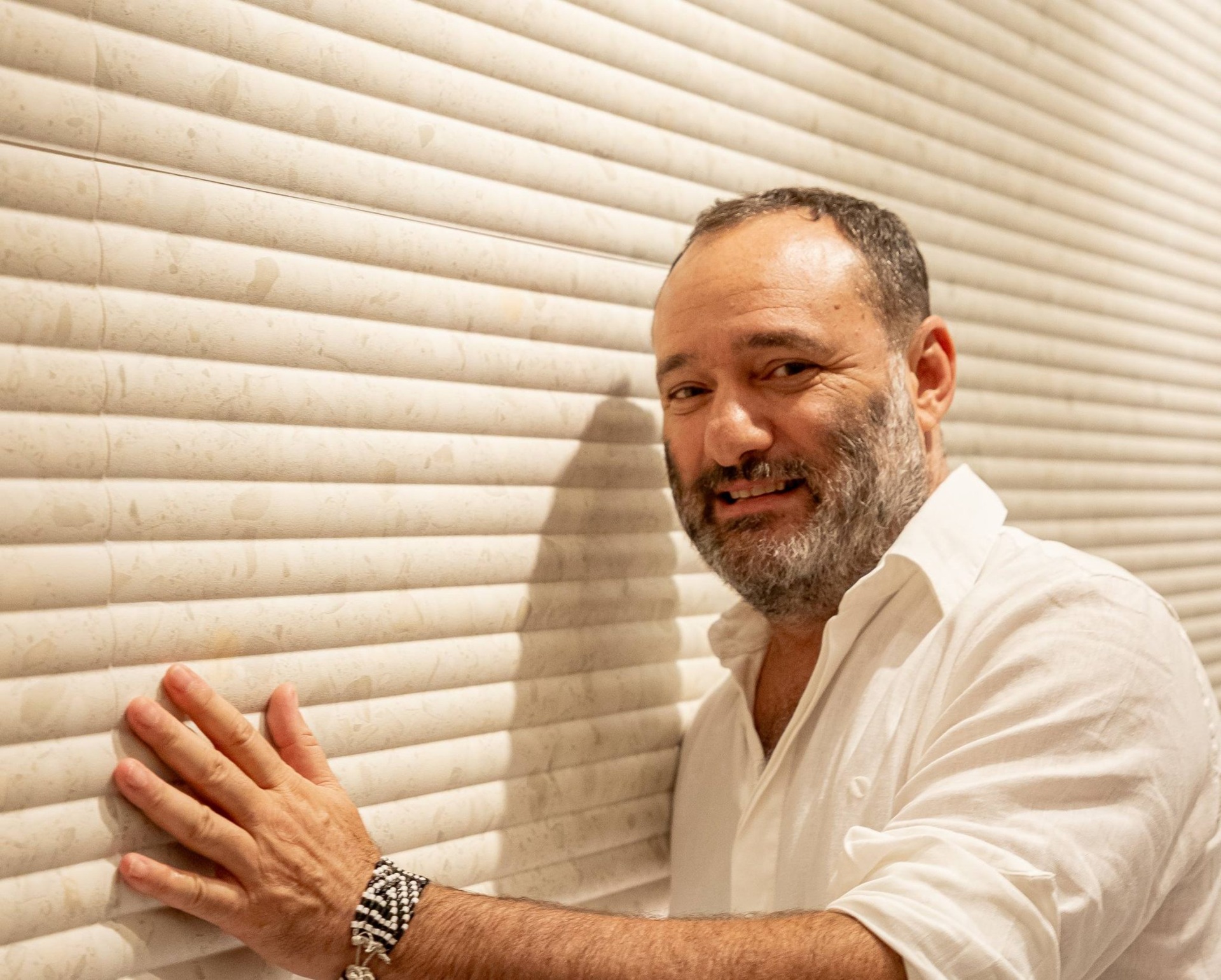 Marcelo Rosenbaum com camisa branca em frente a parede com cerâmica com relevo