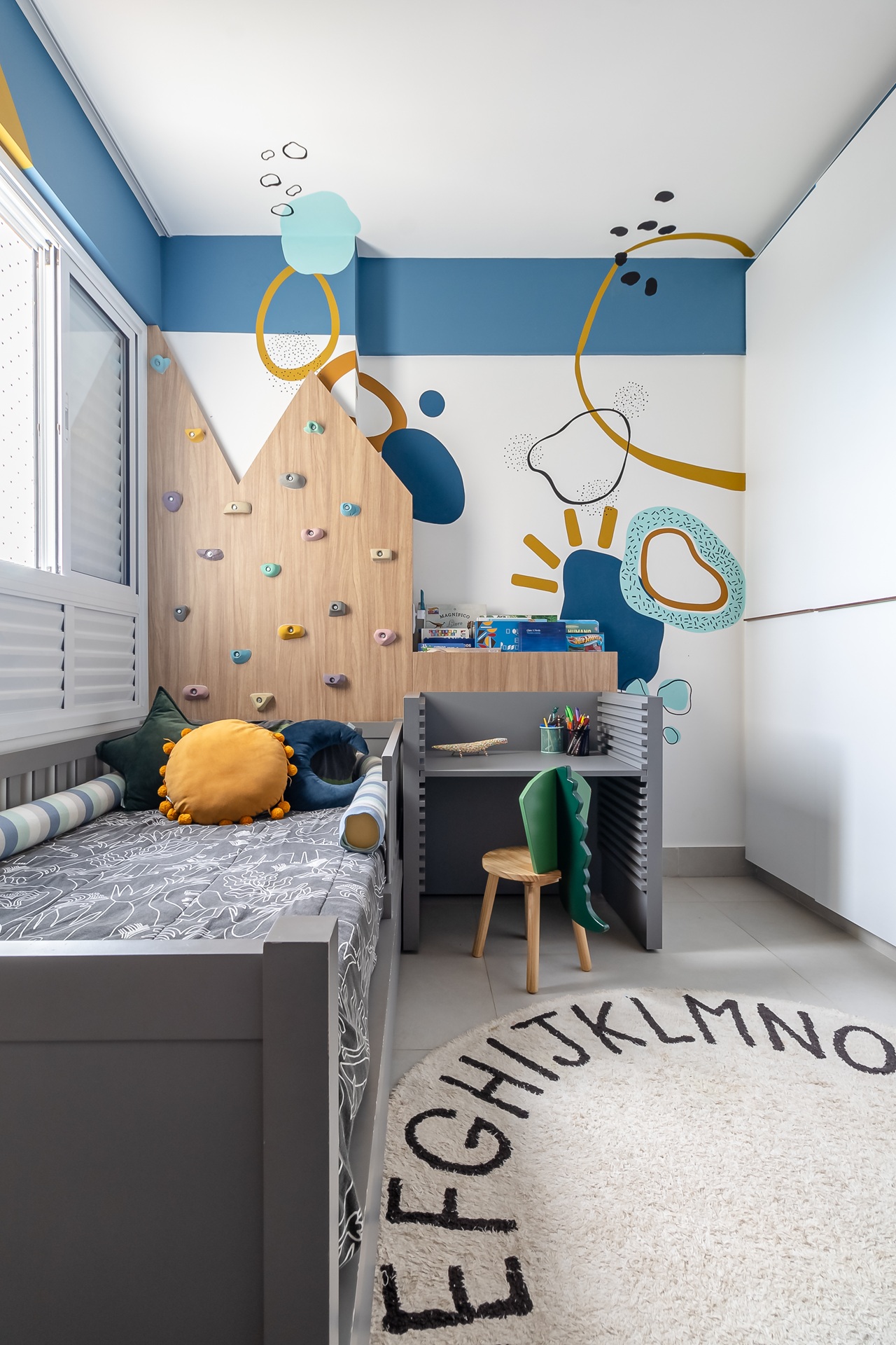 Quarto infantil de menino com parede de escalada, parede com formas orgânicas e cadeira com rabo de jacaré