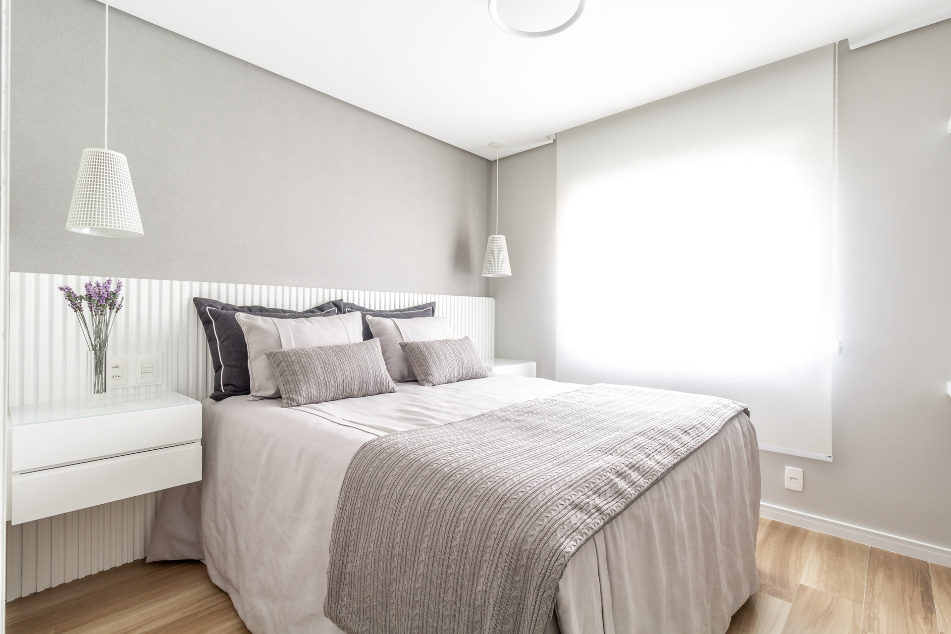 Quarto simples com cama de casal, piso amadeirado e cabeceira ripada branca
