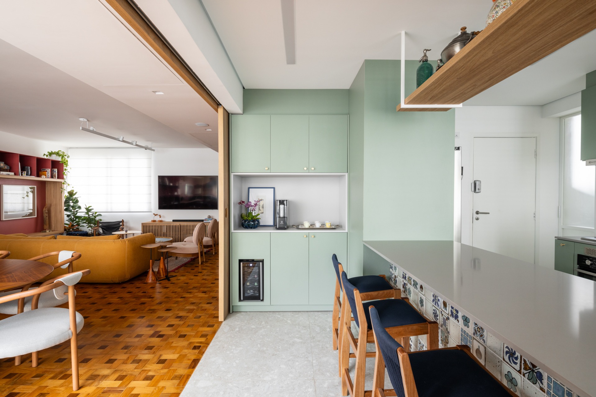 Imagem revela dois ambientes de uma residência: parte da sala de estar de estilo vintage e paleta de cores em tons terrosos; e parte da cozinha, de estilo mais moderno, em tons claros