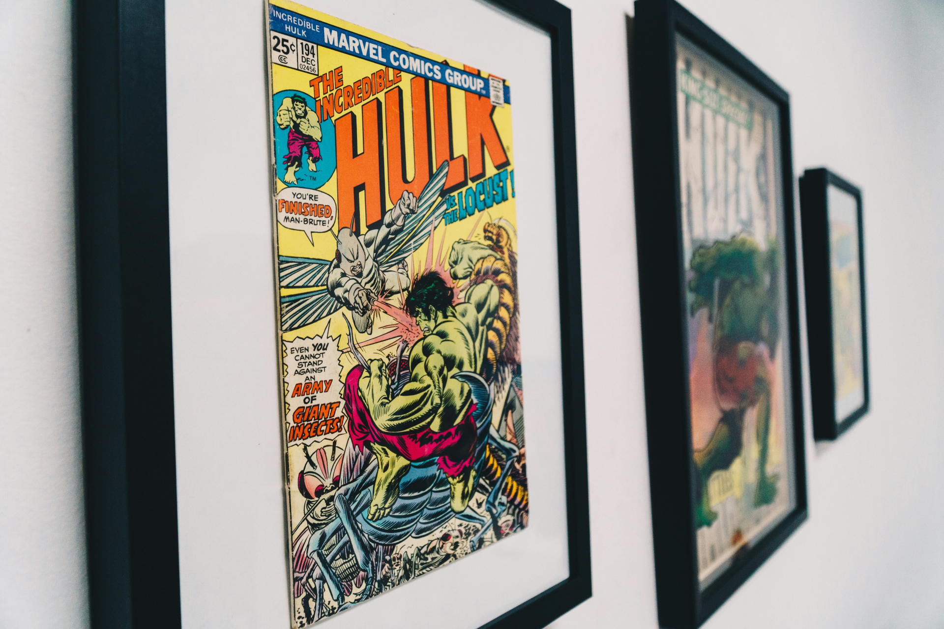 Parede branca decorada com quadros que contêm capas de quadrinhos da Marvel. O quadro principal exibe a capa de 