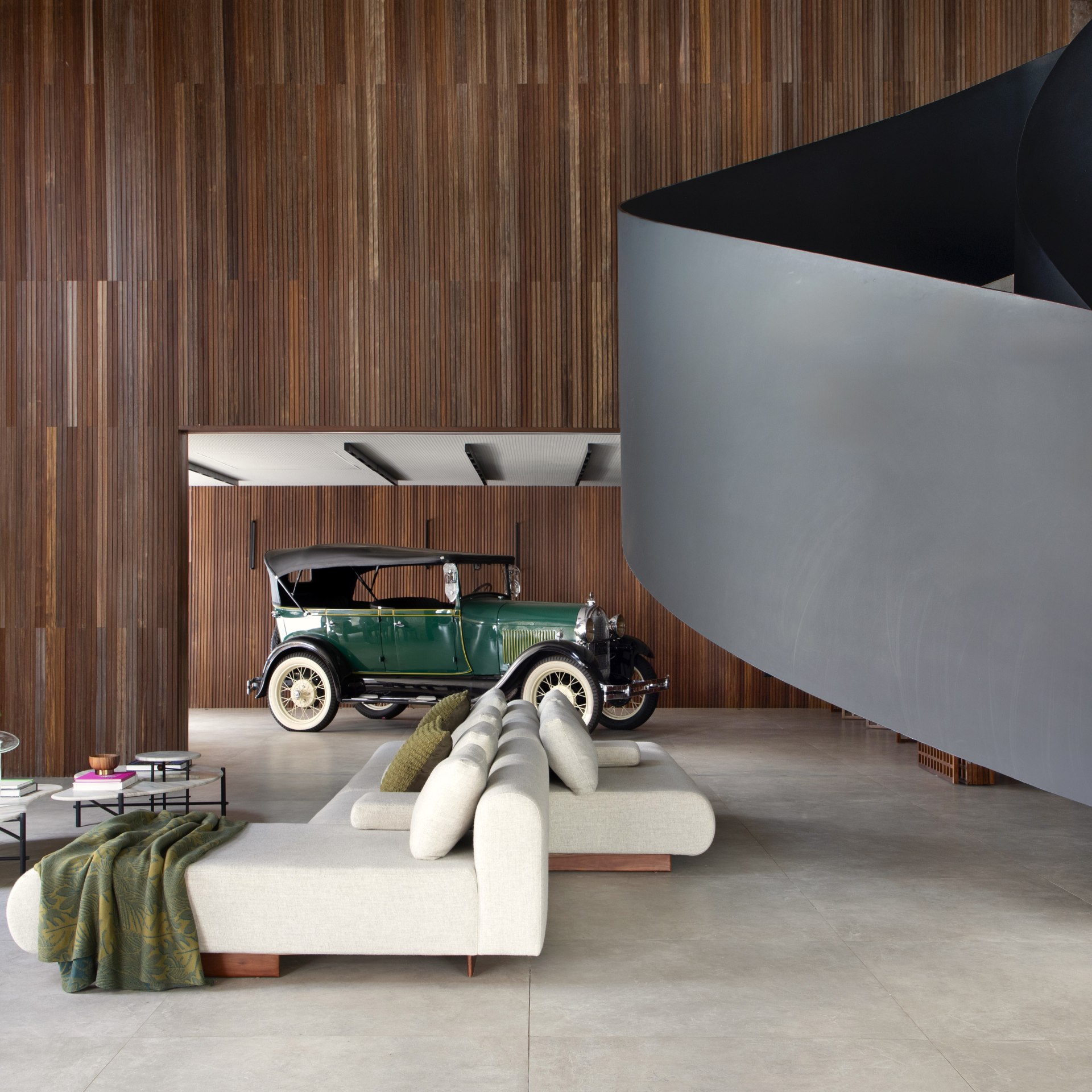 Sala de estar que apresenta uma escada em espiral e um carro antigo e verde estacionado ao fundo do ambiente