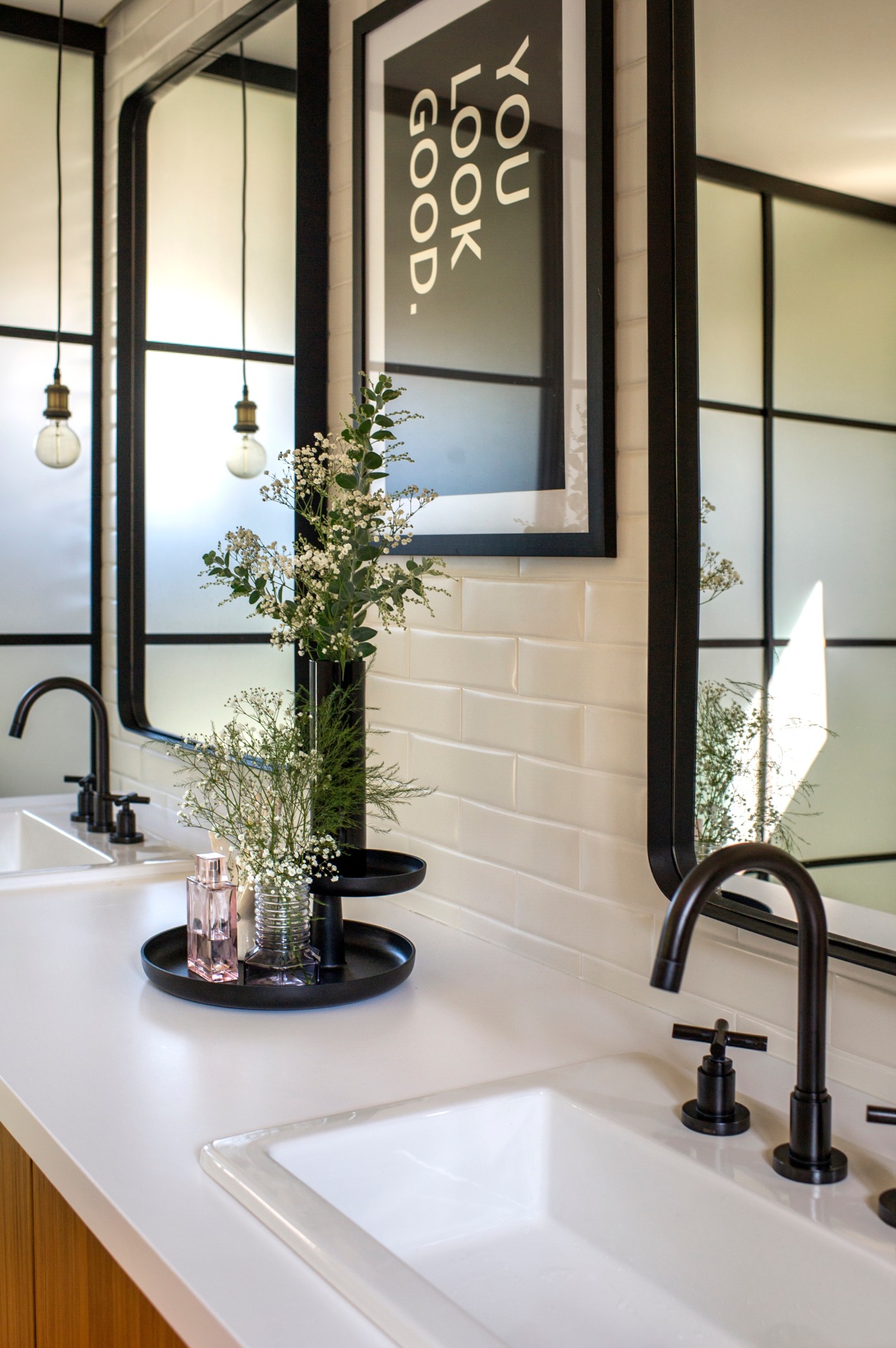 Bancada de banheiro no estilo industrial, com azulejos de metrô, metais pretos e lâmpadas de filamento