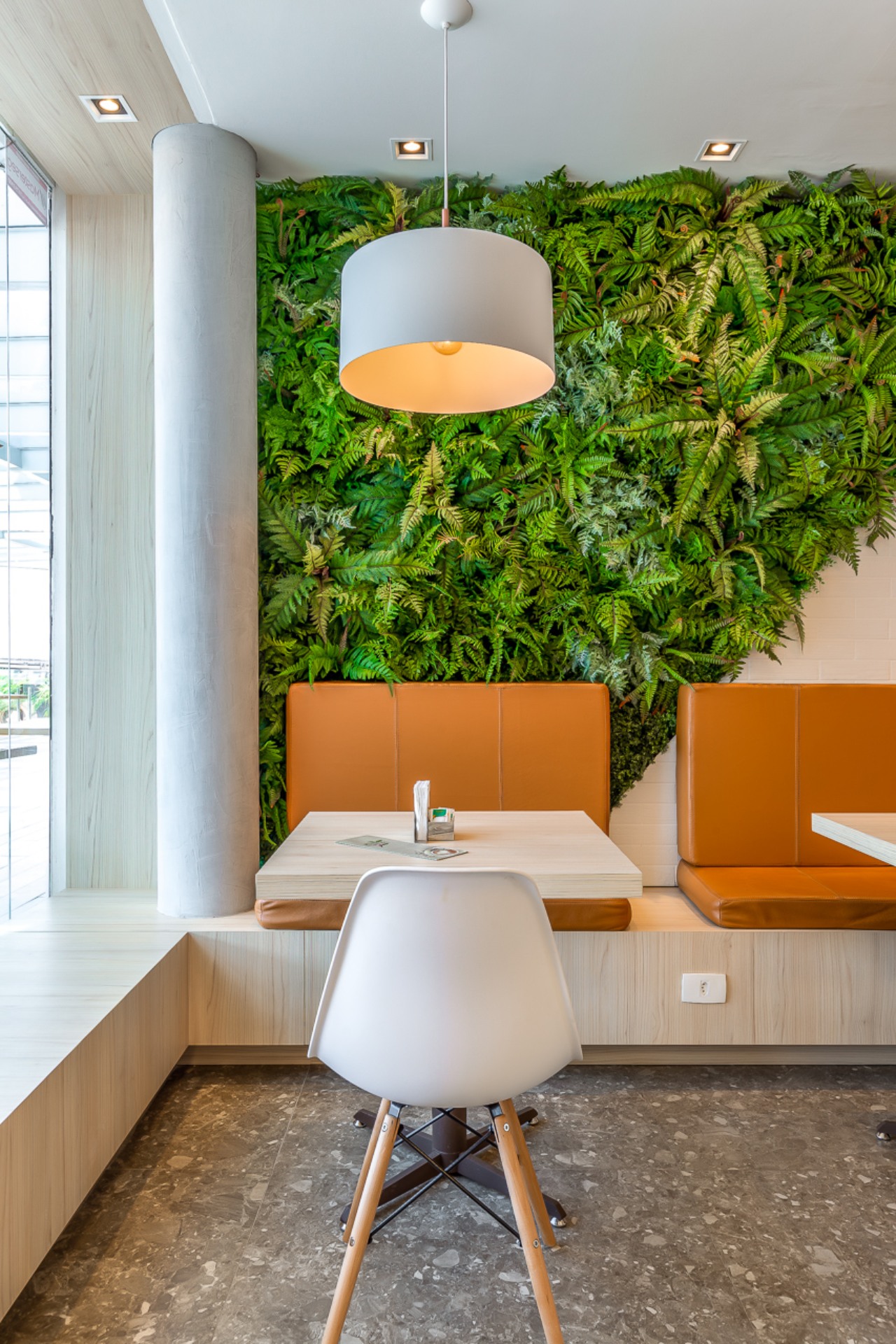 O ambiente combina elegância e simplicidade, com cadeiras de design leve, tons claros, e toques naturais como a parede verde e o piso de concreto