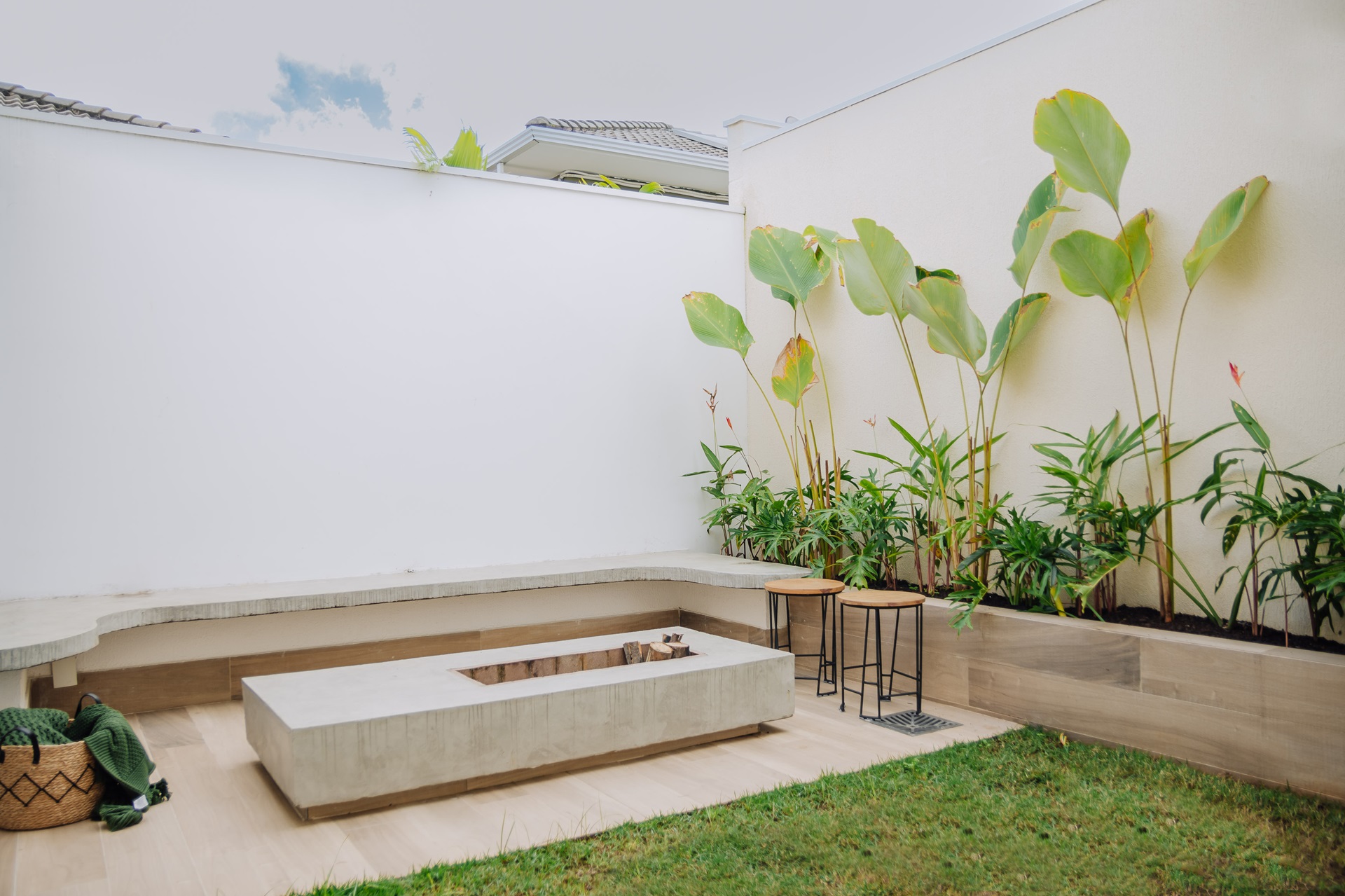 Imagem de um quintal compacto com jardim, banco em alvenaria e fire pit retangular no centro