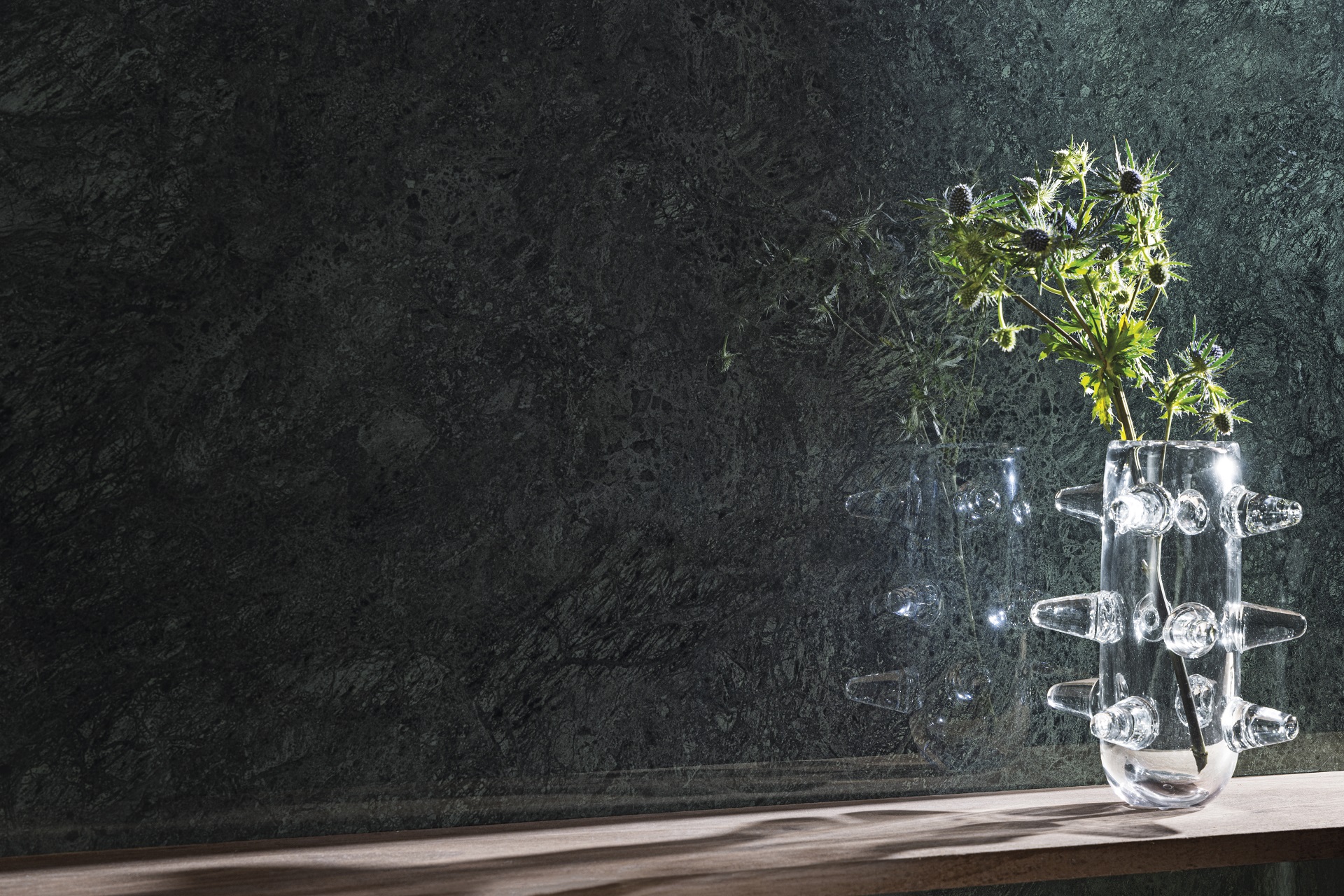 Detalhe de parede revestida com porcelanato que recria mármore verde da Portobello, com mesa e vaso de folhas em frente