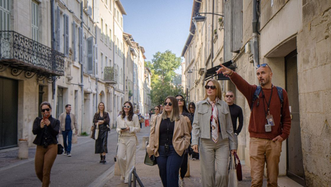 Grupo de turistas sendo guiado por homem em rua estreita com prédios históricos.