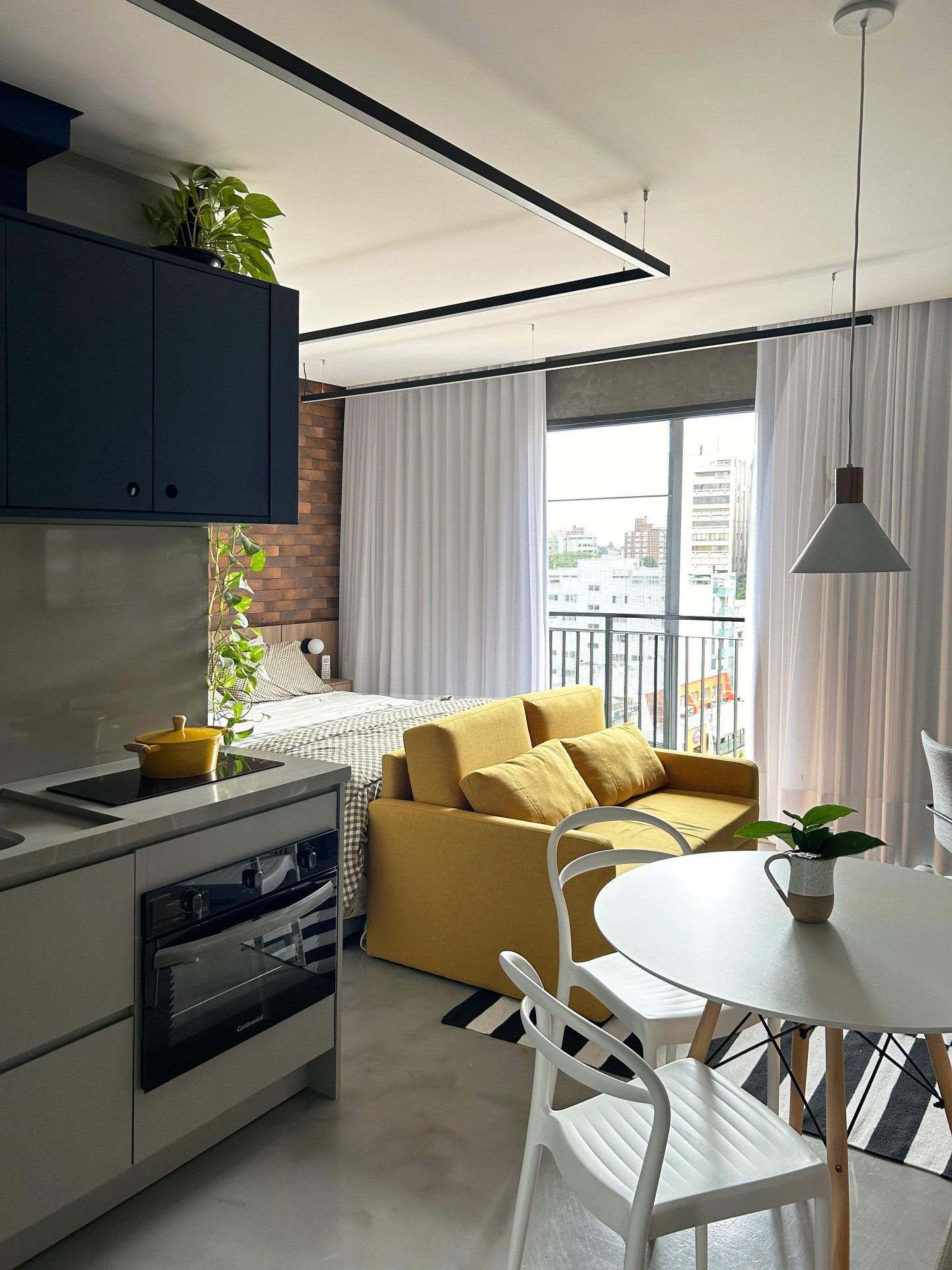 Microapartamento com sala, cozinha e quarto integrados. A paleta de cor consiste em amarelo, cinza e azul