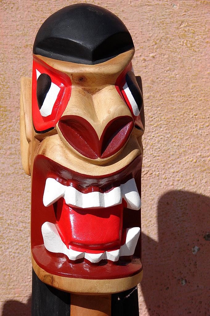 Carranca de madeira com cabeça que mistura figura humana e animal, com destaques pintados em branco, vermelho e vinho
