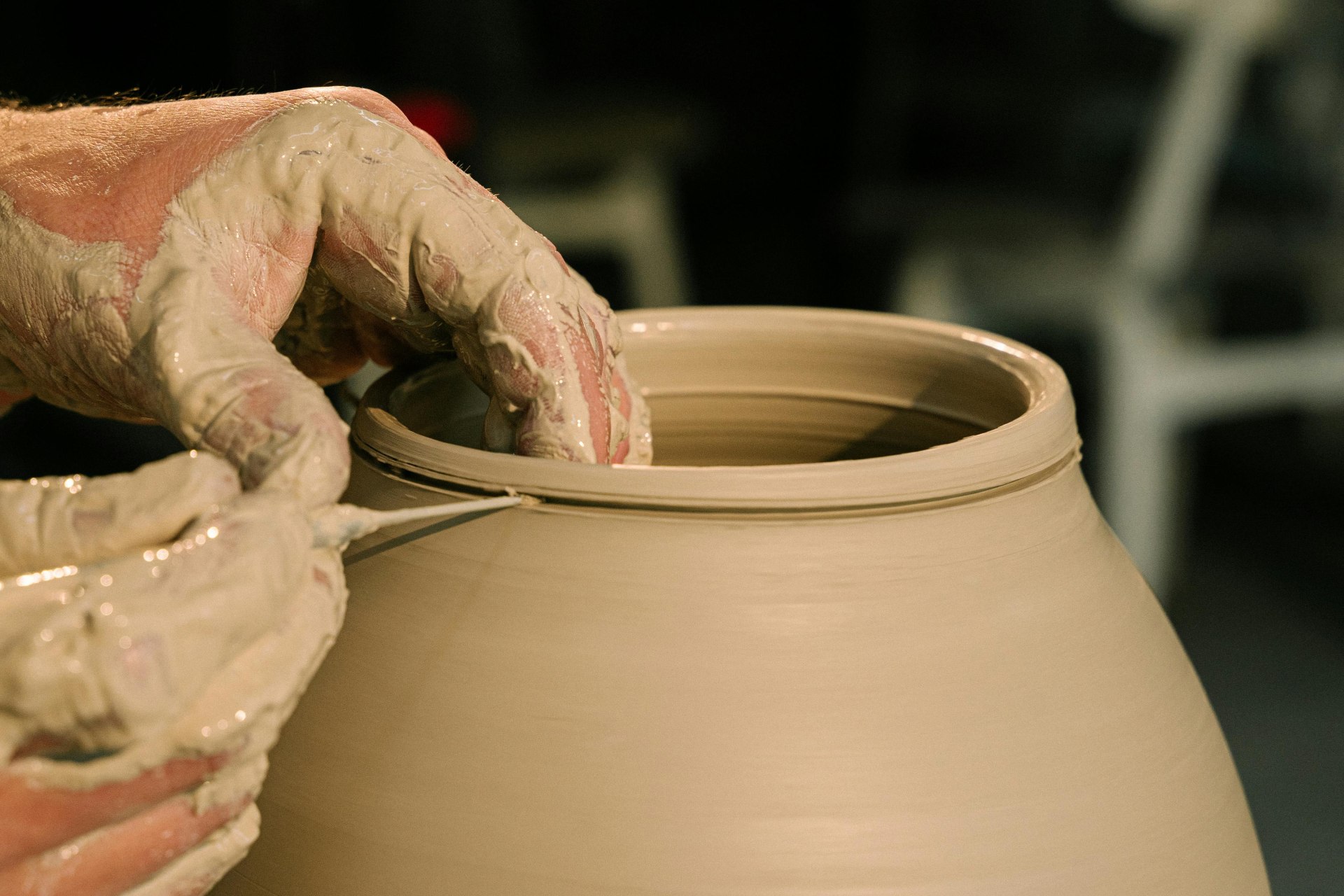 Mãos modelam o barro para a produção do que aparenta ser um vaso