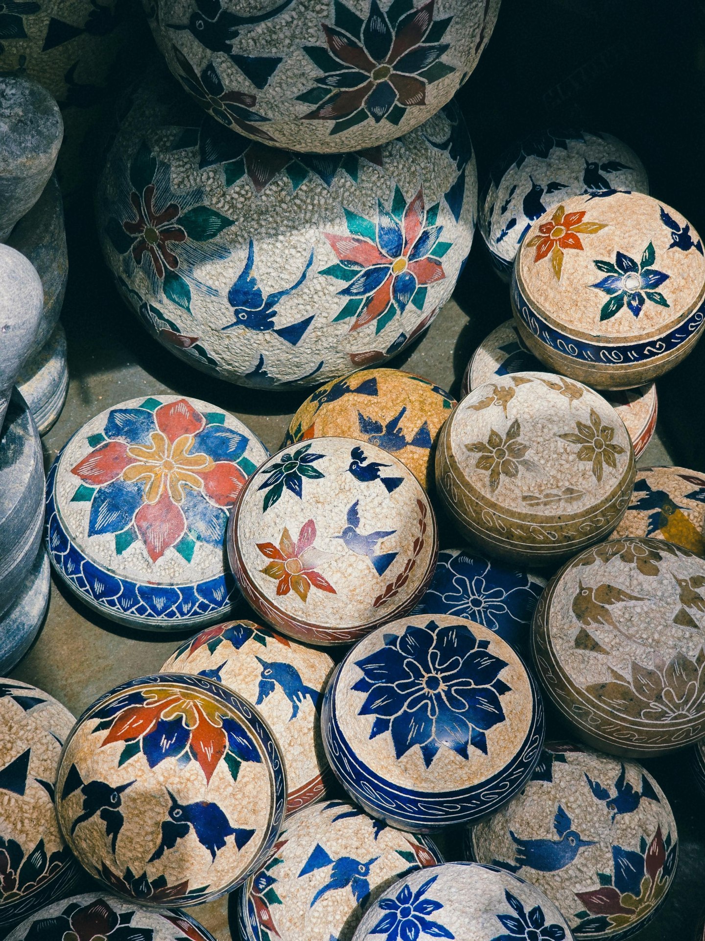 Potinhos arredondados de pedra-sabão decorados com pinturas de flores e pássaros em cores vemelha, amarela e azul