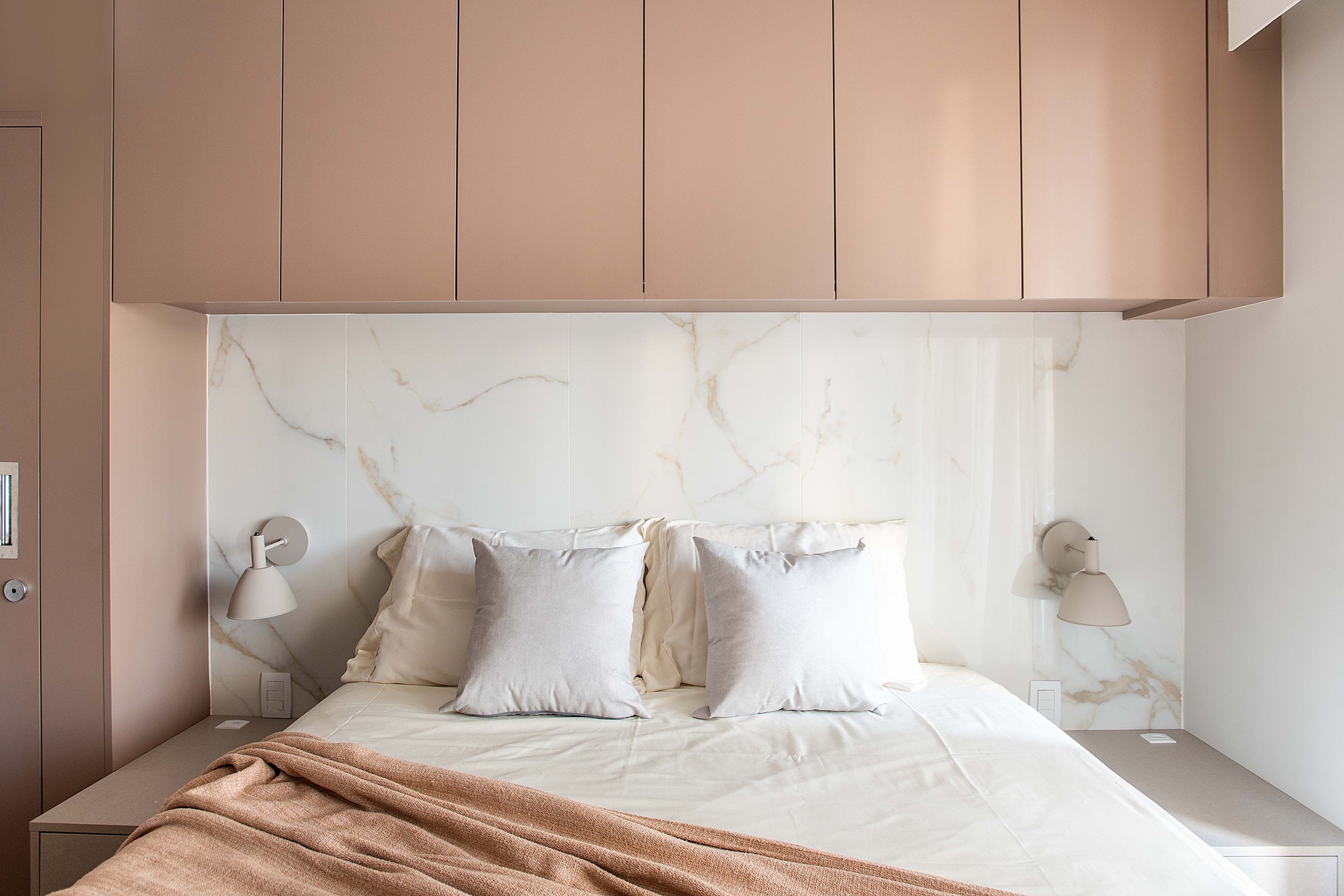Quarto com cama de casal e cabeceira em porcelanato que reproduz mármore