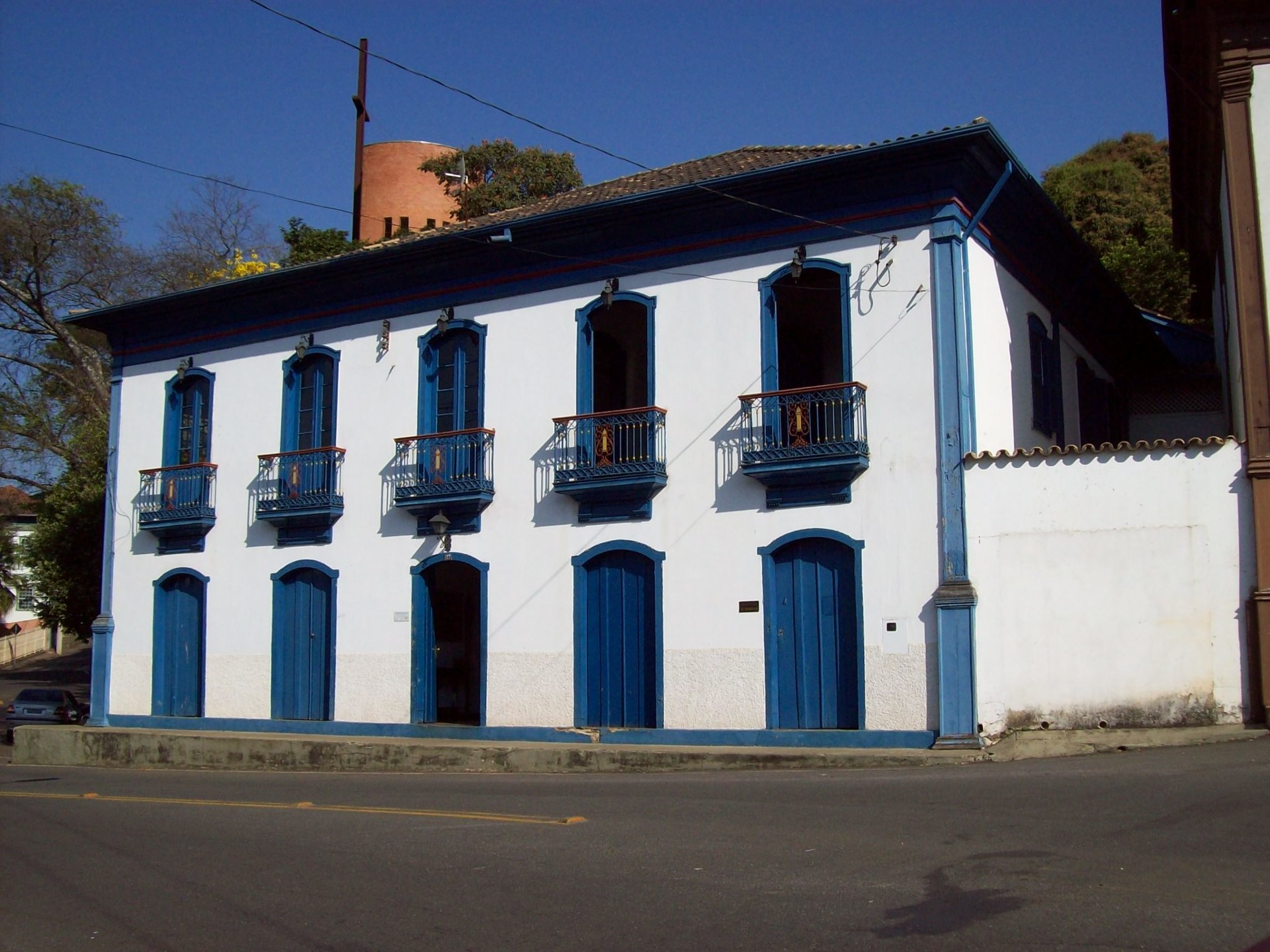 Fachada da Casa de Drummond, de estilo colonial, com paredes brancas e uma série de portas de madeira pintadas de azul