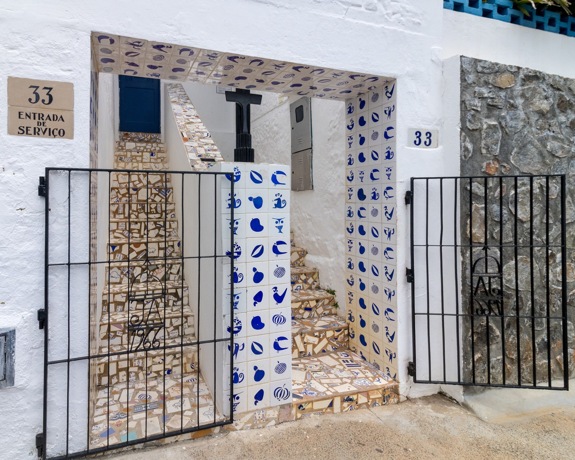Entrada da Casa do Rio Vermelho. Fachada branca, com portões pretos baixos que dão para duas entradas com escadas revestidas de mosaico de azulejos