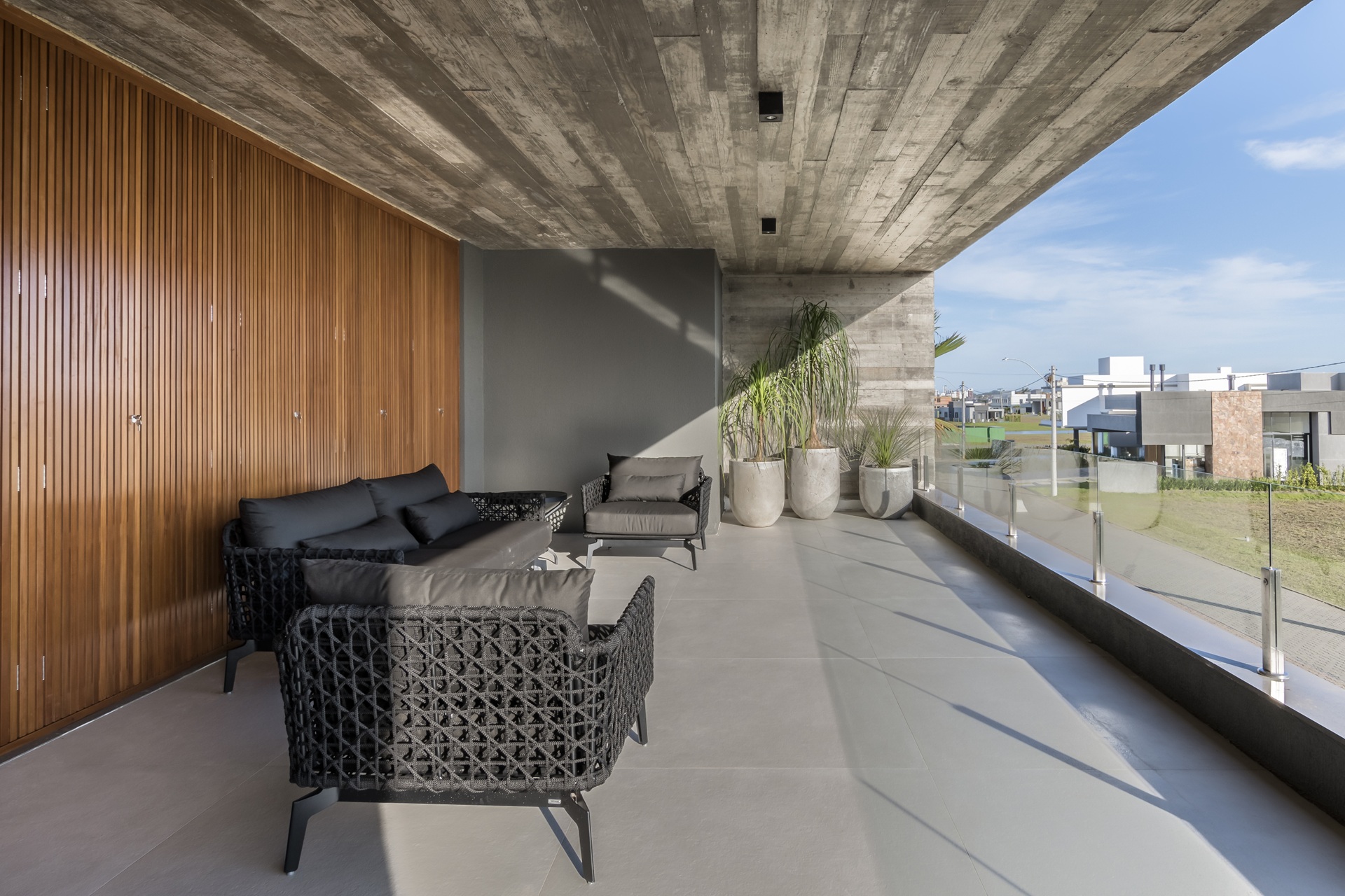 Varanda com teto em concreto aparente e piso em porcelanato que reproduz concreto