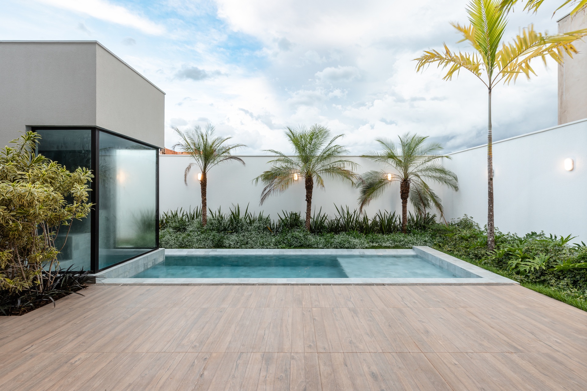 Jardim com piso amadeirado, piscina e paisagismo