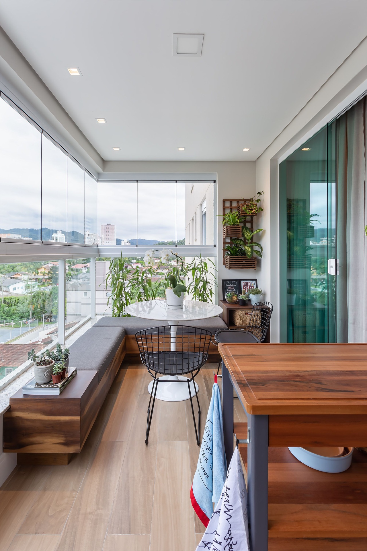 Área externa de um apartamento com bancos de madeira e decoração com vasos e plantas.