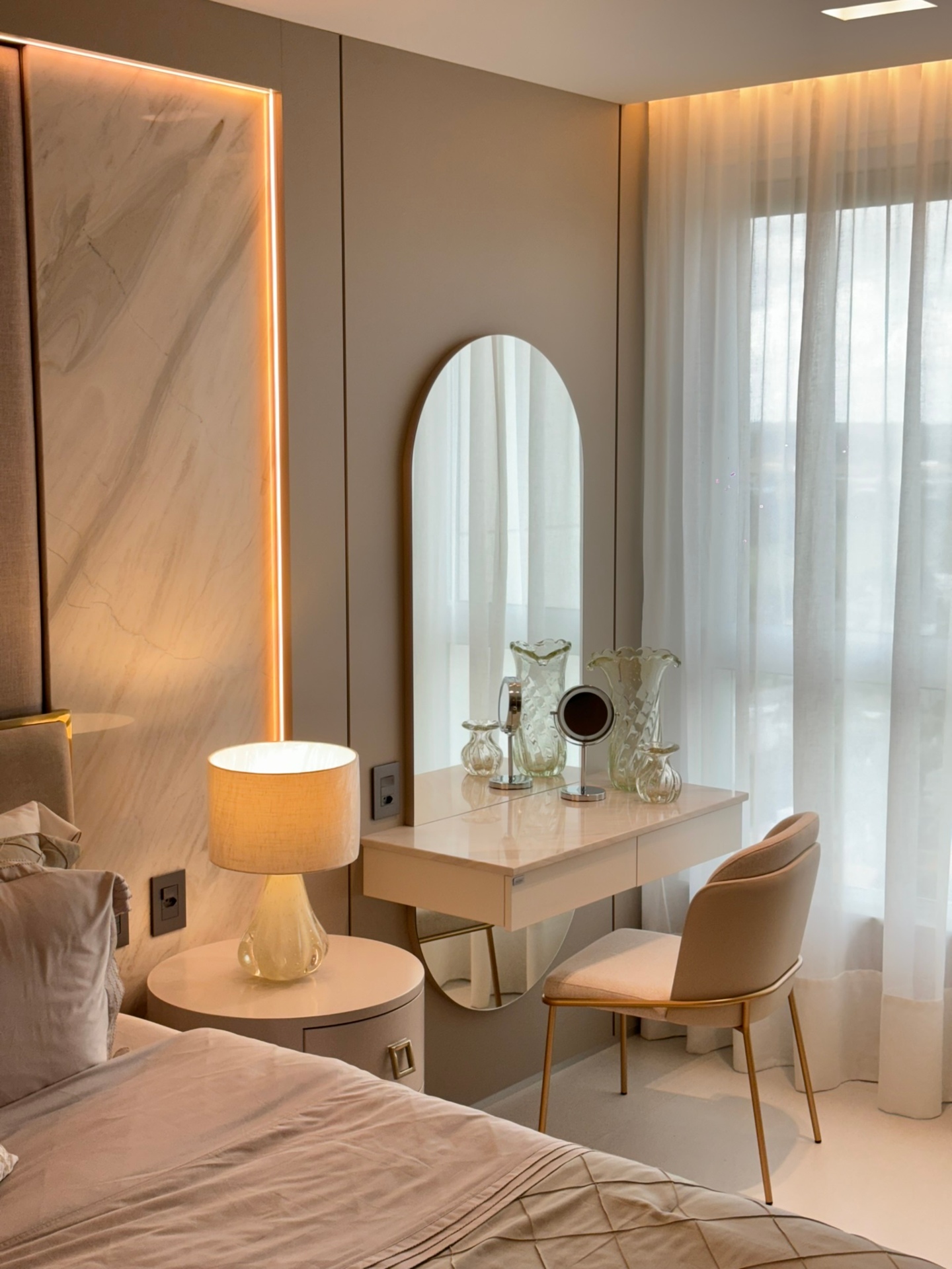 Quarto com penteadeira em tons neutros, espelho grande, madeira clara, bancada branca e iluminação embutida